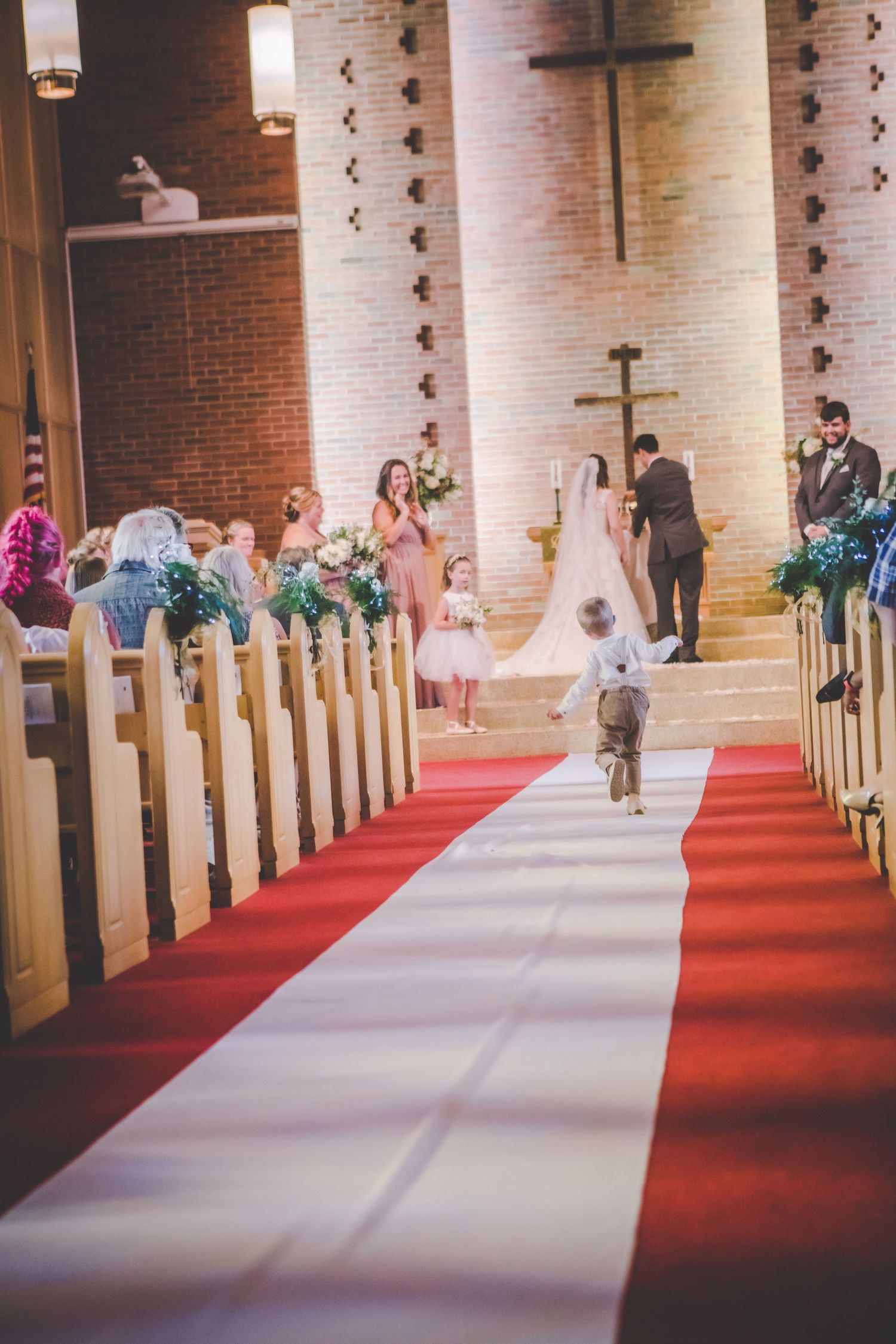 Wedding aisle decorated with white runner and red carpet in a brick church sanctuary.