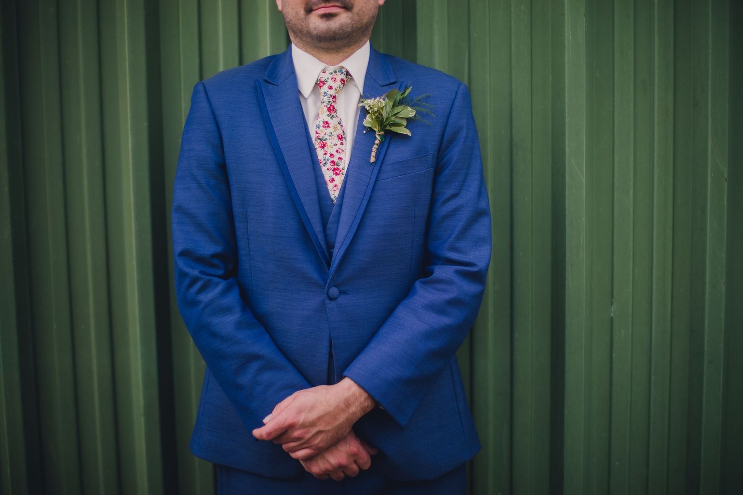 Groom and groomsmen in bright blue suits stand before green metal wall.