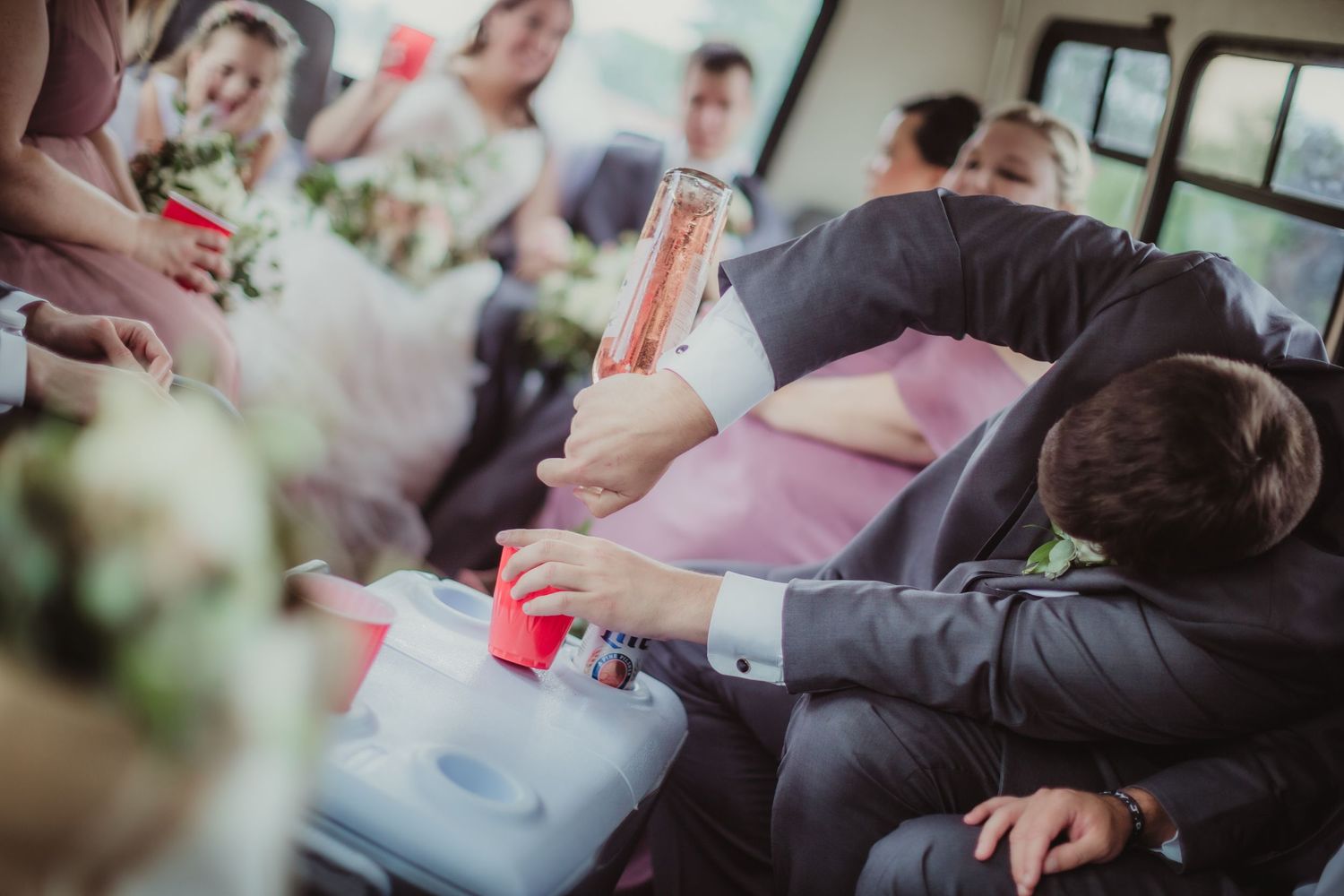 Guest in formal attire serves drinks from a cooler during wedding transportation.