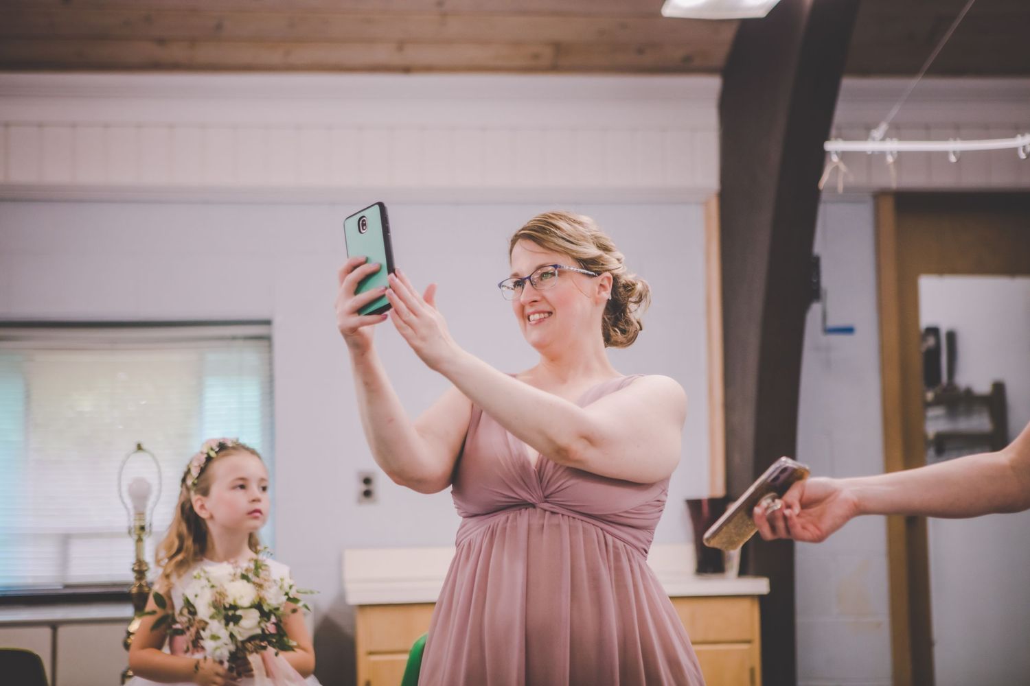Person in dusty rose dress taking selfies during wedding celebration.