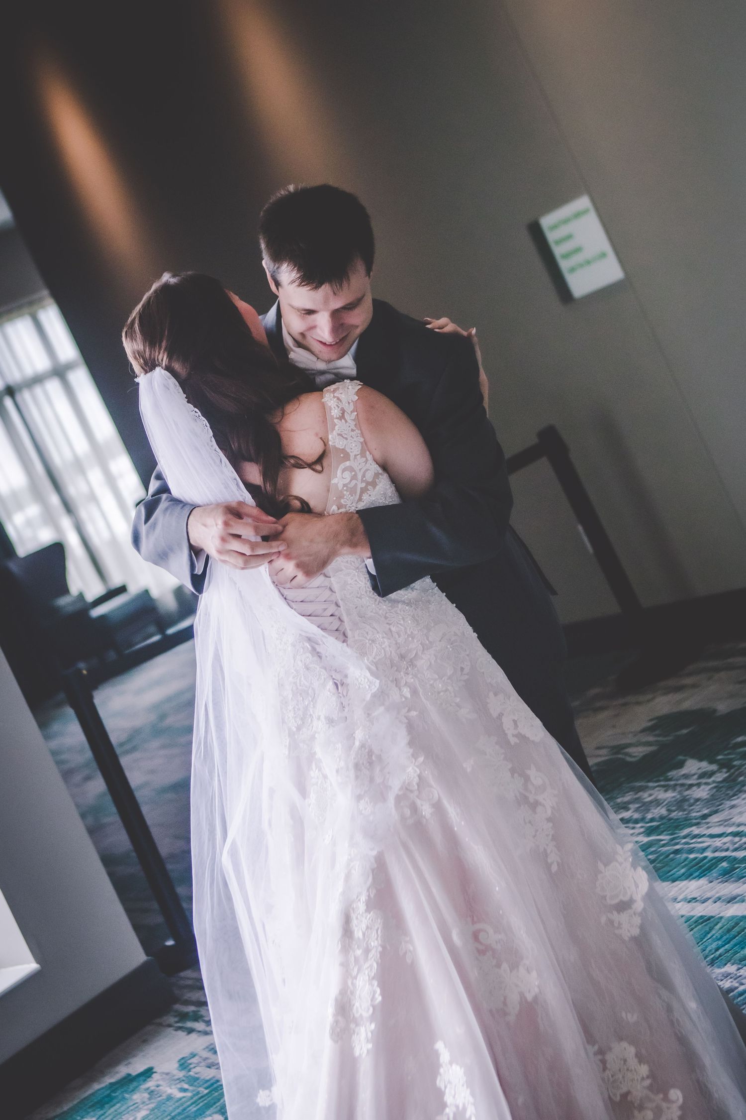 The couple shares a romantic dance in their wedding attire by a window.