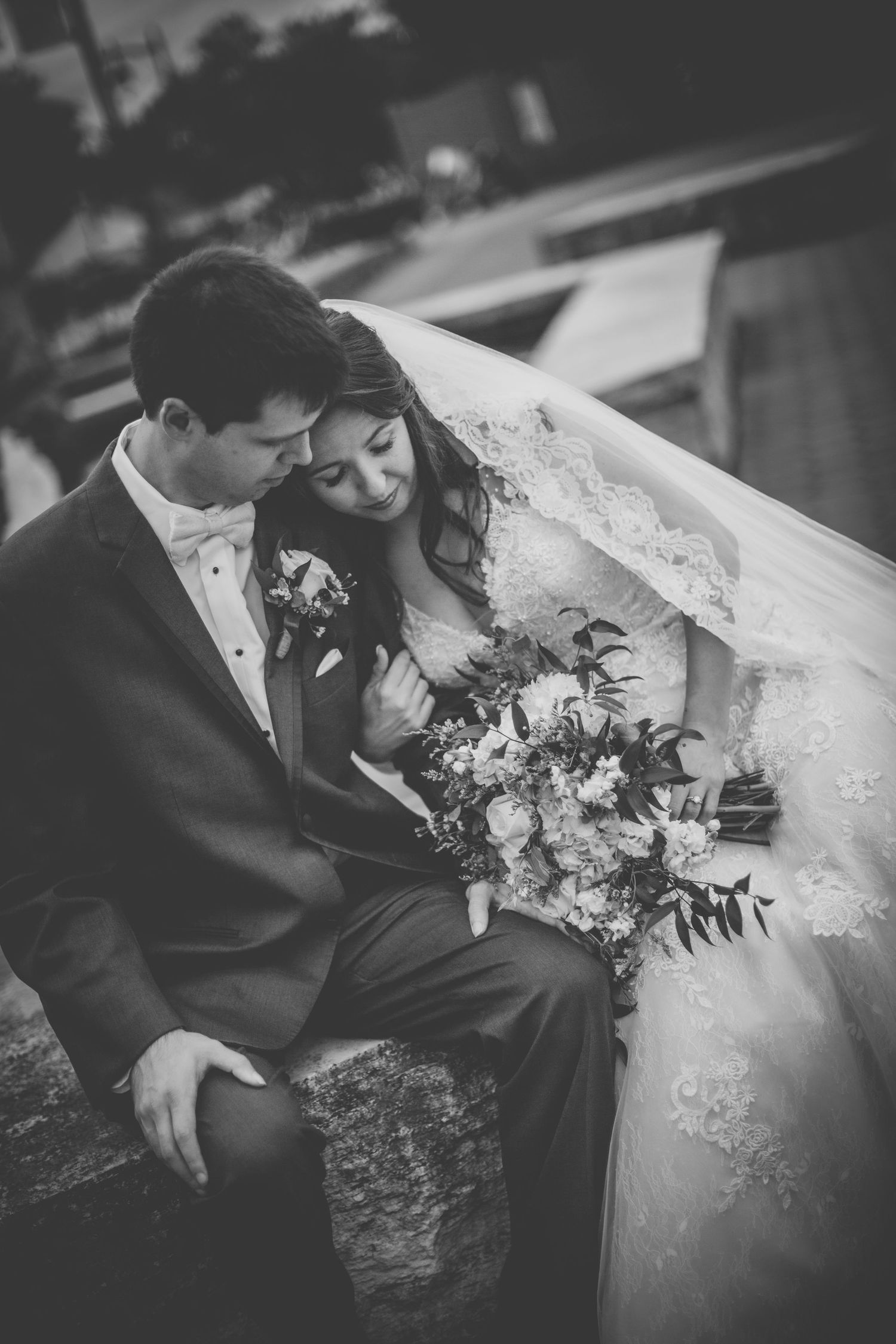 Black and white wedding portrait shows tender moment between newlyweds on stone steps.