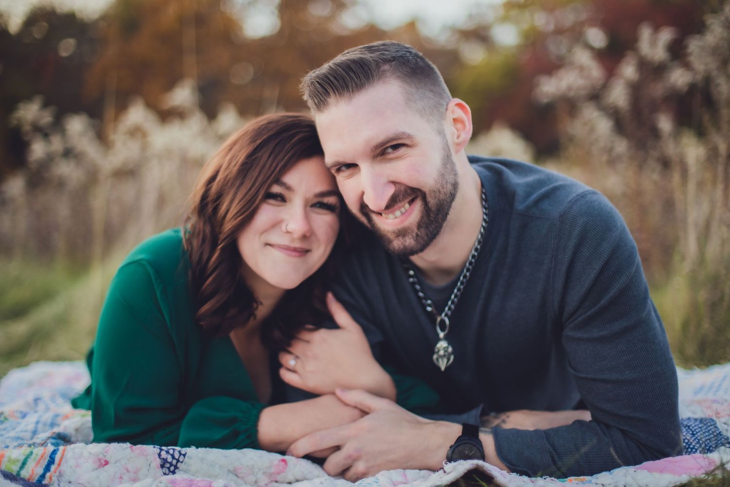 Happy couple sharing laughs while laying on blanket in outdoor fall setting.