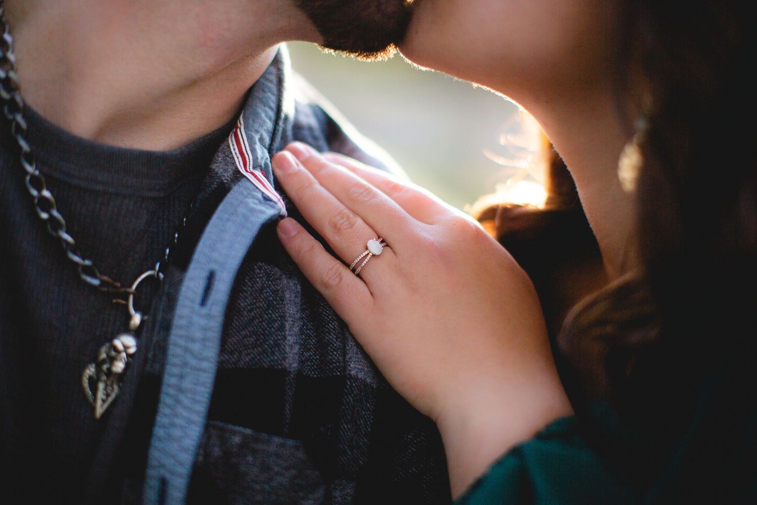 Close-up of hands with engagement ring against blue plaid shirt.
