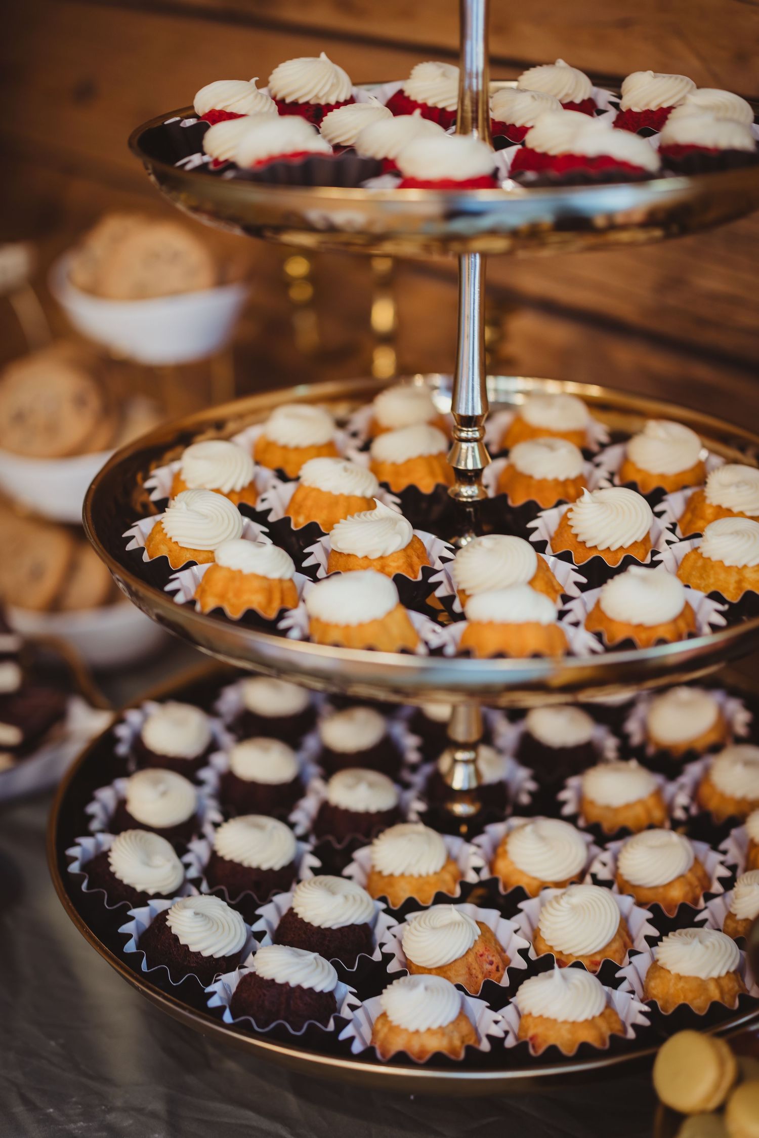 Three-tiered gold dessert stand filled with mini bundt cakes and cupcakes topped with white cream frosting.