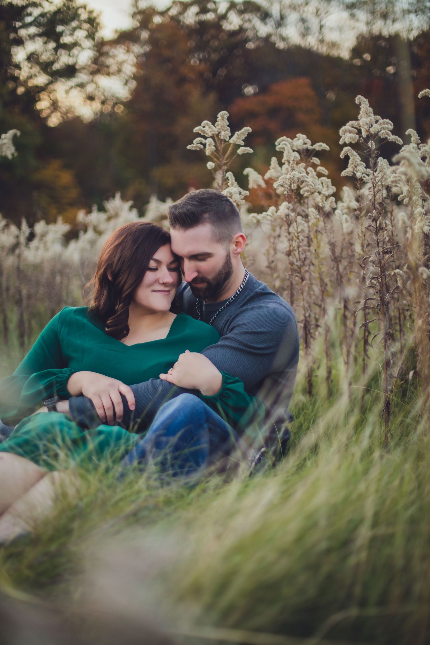 Intimate portrait of couple nestled in tall grass during autumn photoshoot.