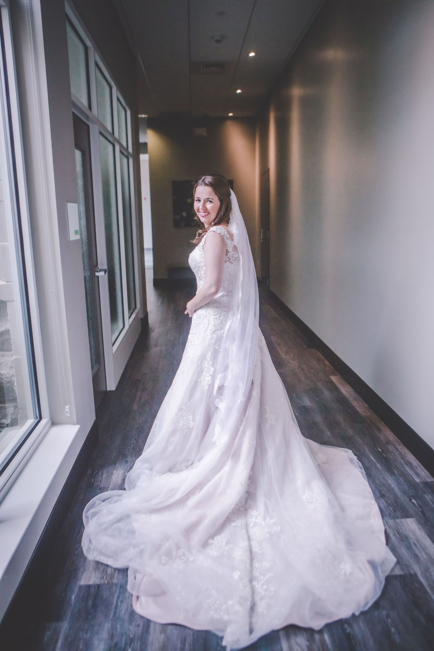 Romantic bridal photo showing a flowing train and veil against floor-to-ceiling windows.