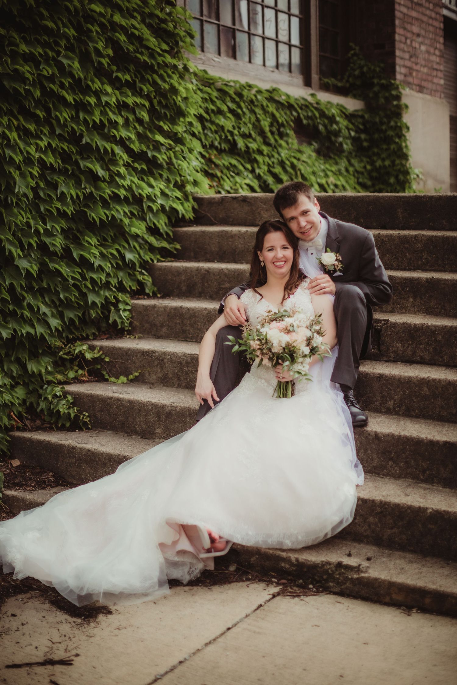 Newlyweds pose on ivy-covered stone steps for a romantic wedding portrait.
