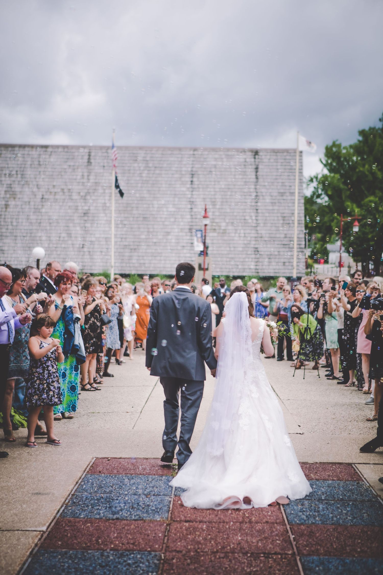 Wedding couple walks down red white and blue pathway as guests line both sides watching.