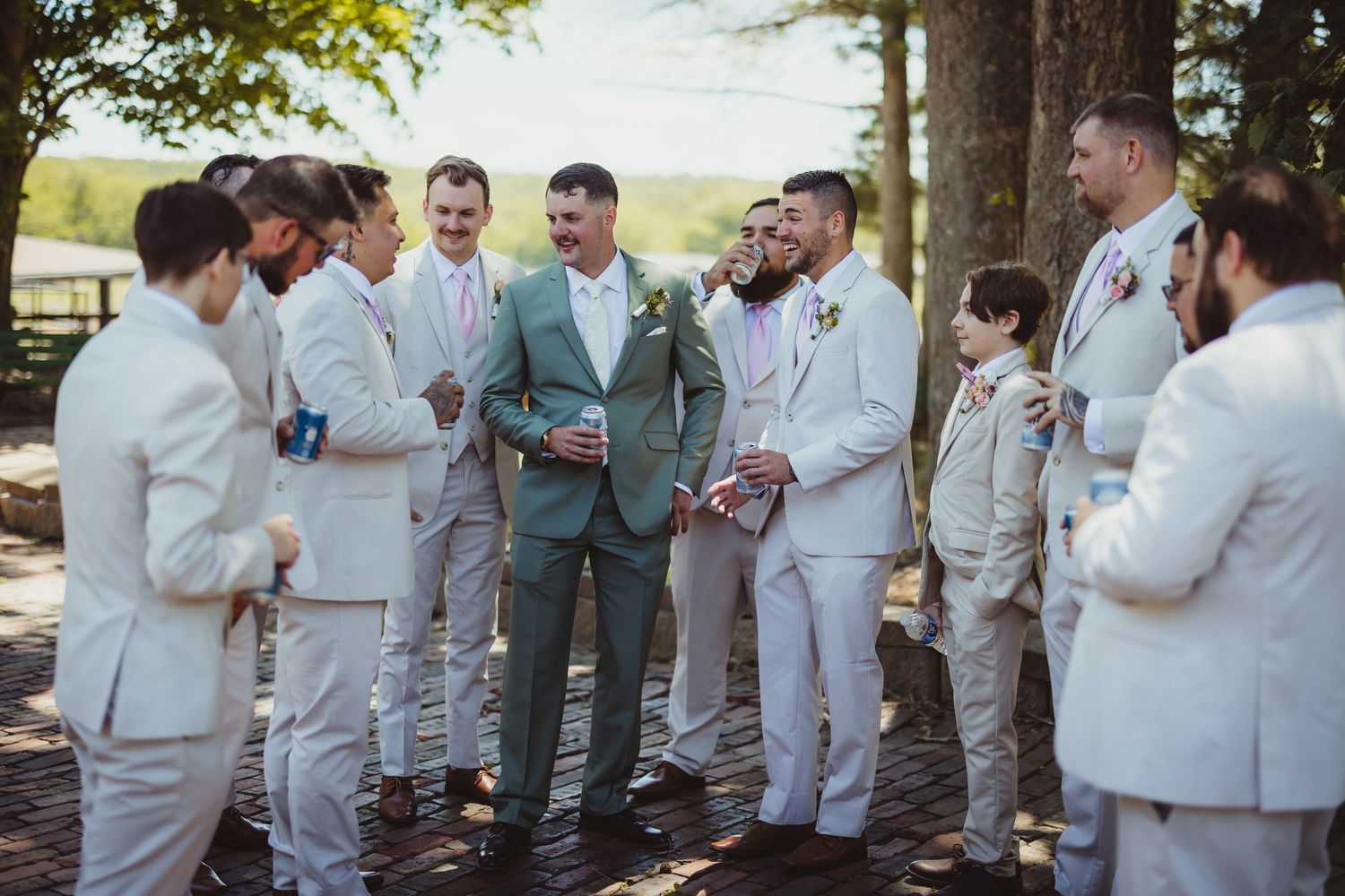 Groom in sage green suit stands with groomsmen in white linen suits at an outdoor wedding celebration.