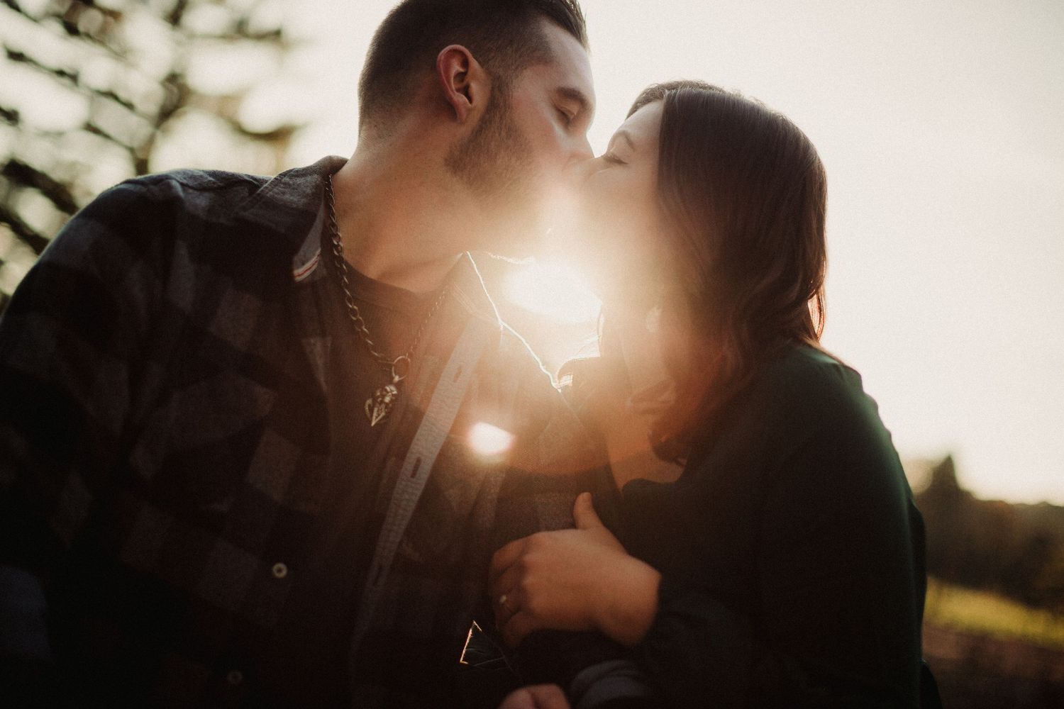 Silhouette of couple embracing with sun flare in background.
