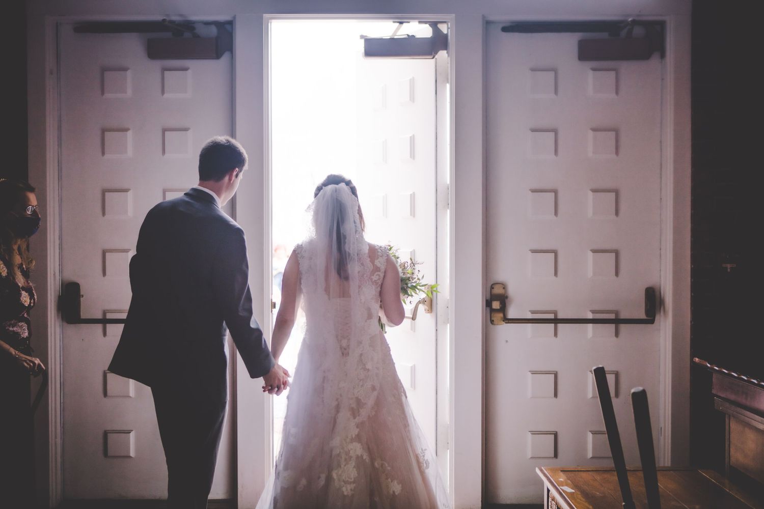 A couple walks hand in hand towards bright church doors on their wedding day.
