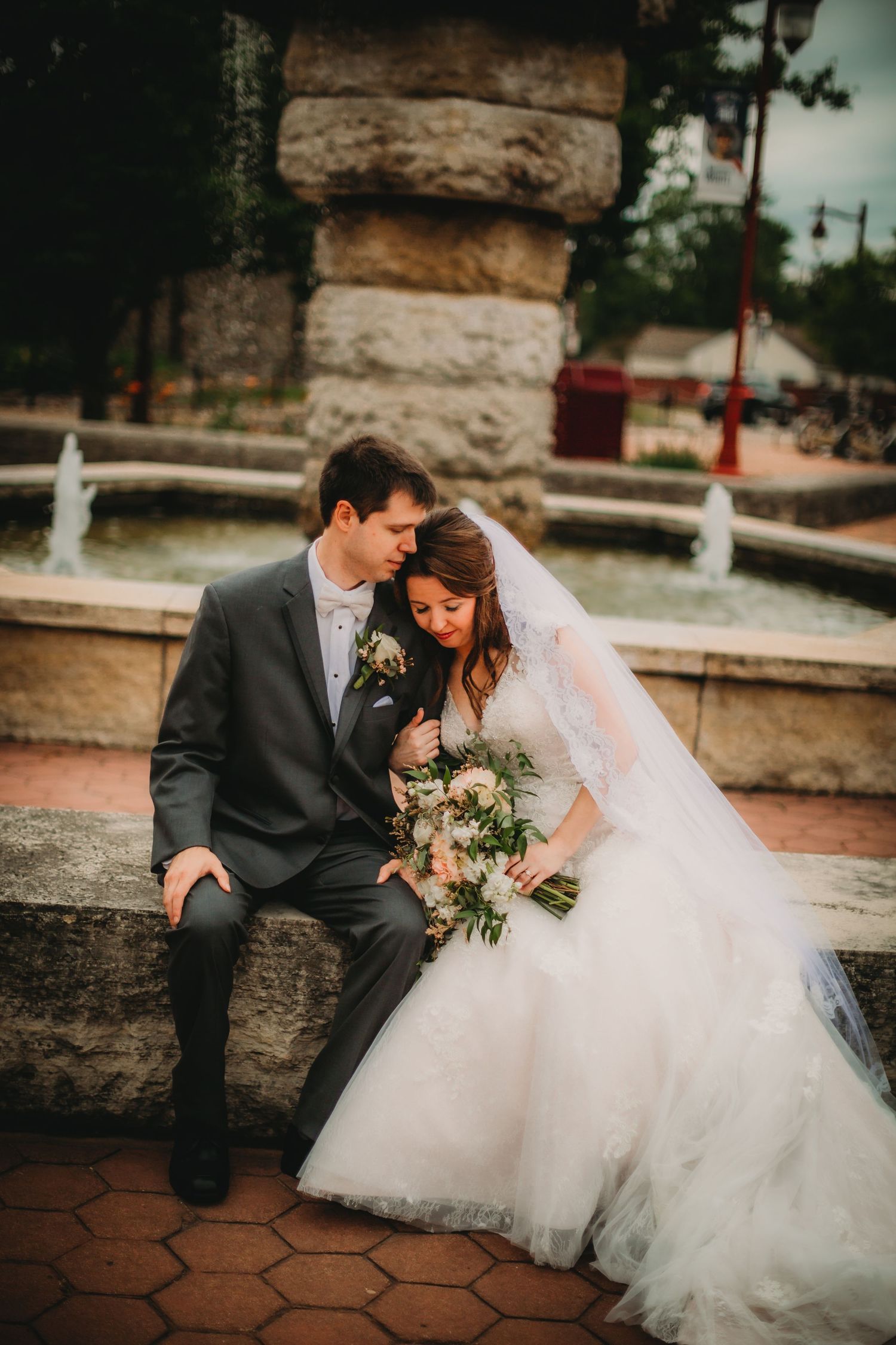 A romantic wedding couple sits together on stone steps holding delicate floral bouquet.