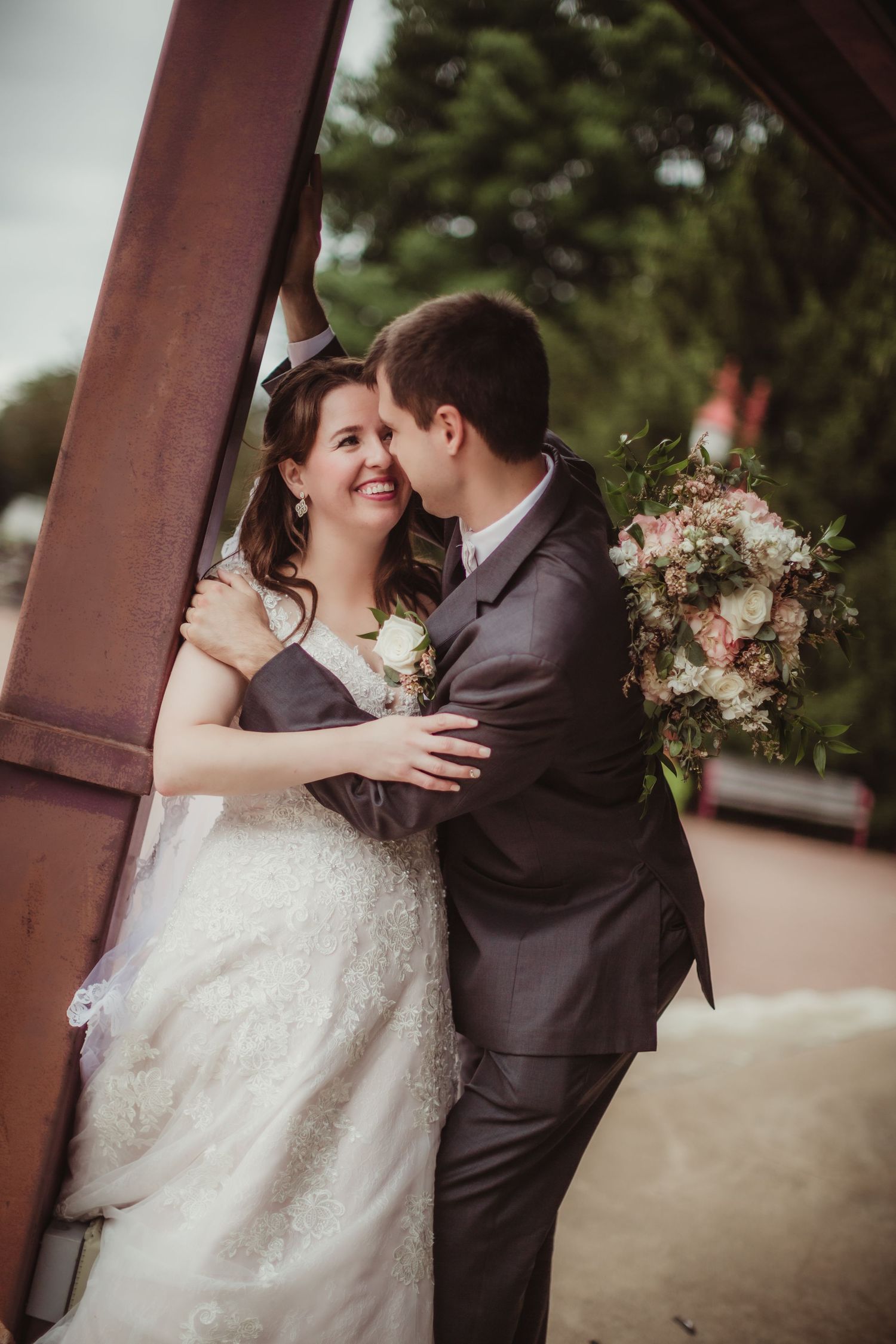 A tender wedding moment captured as newlyweds share an intimate embrace by a rustic pillar.