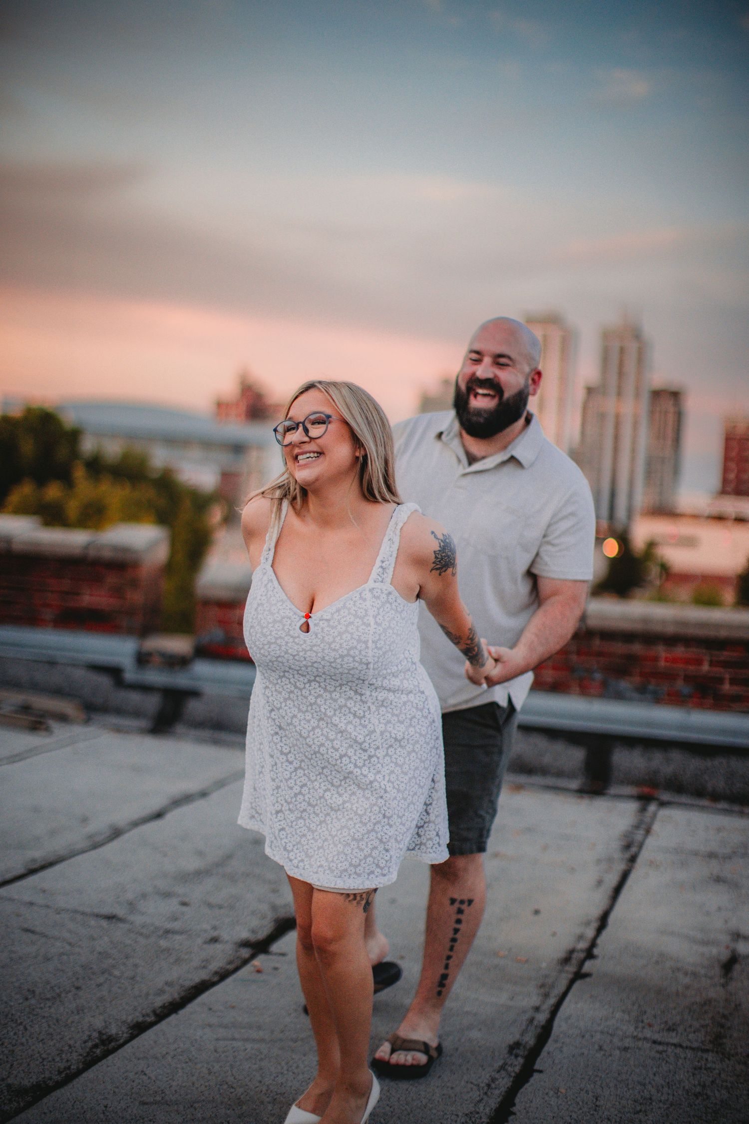 A couple enjoys a sunset moment together on an urban rooftop with city buildings in the background.
