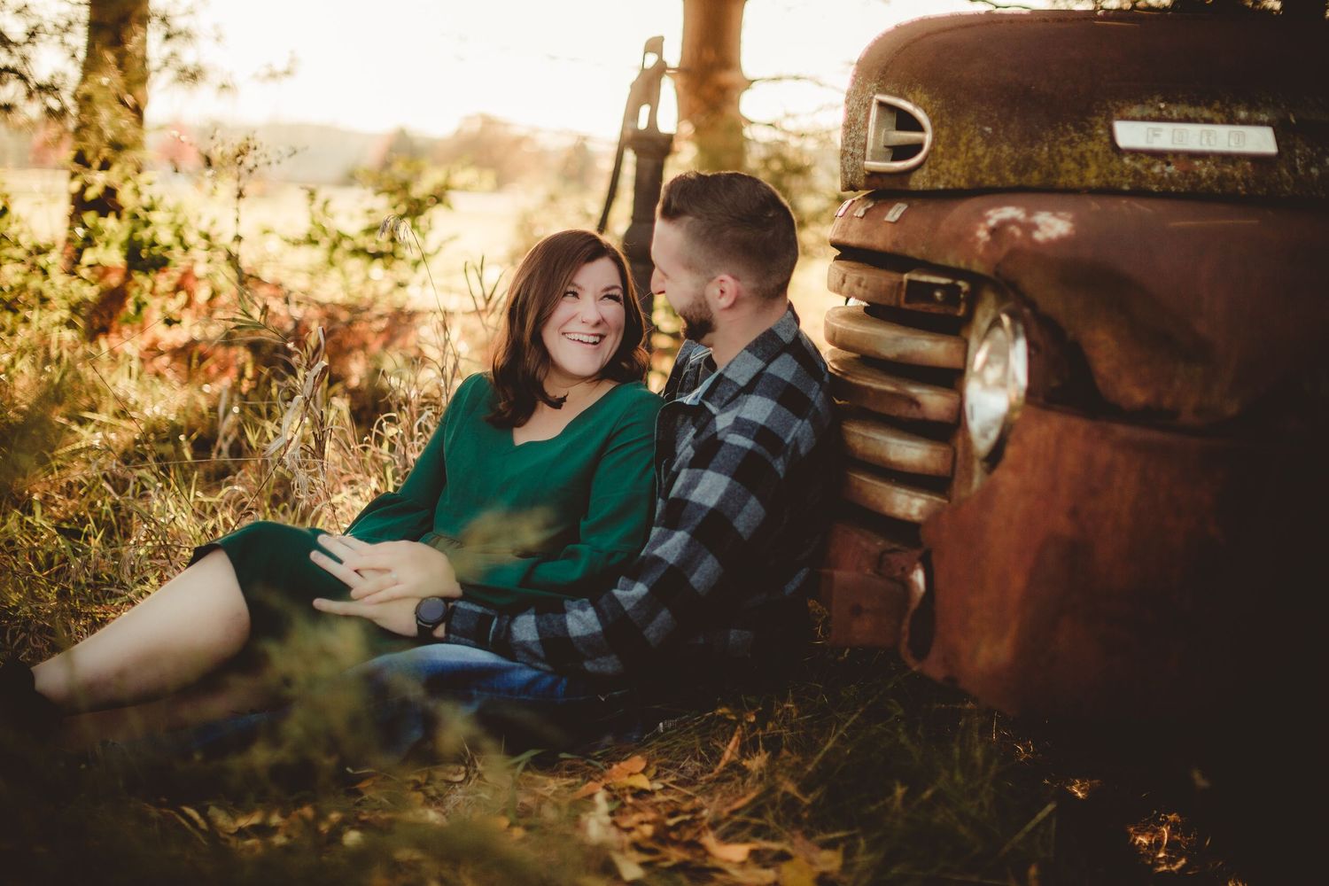 Couple sits together by vintage truck in warm autumn sunlight through trees.