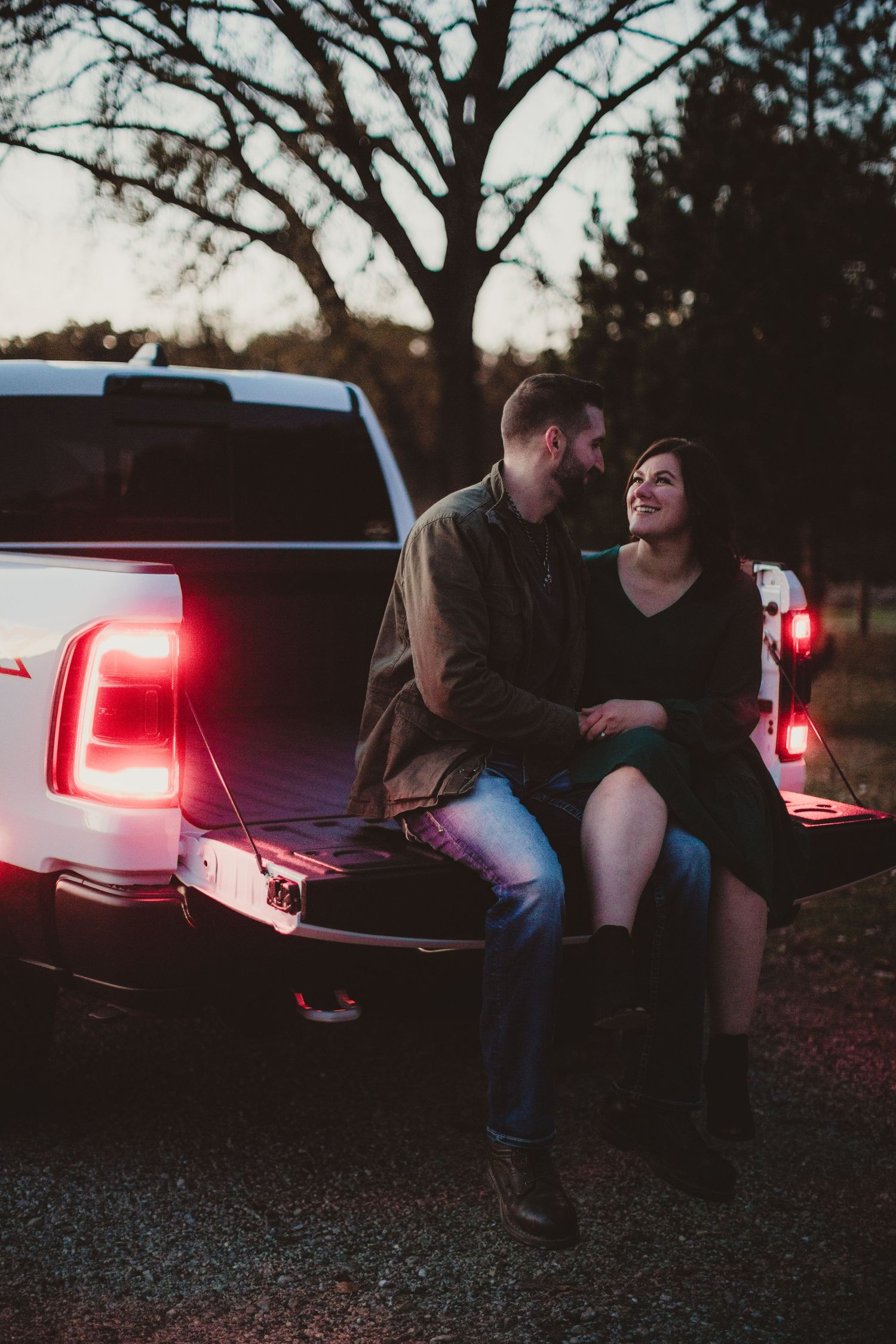 Couple enjoying evening together on pickup truck tailgate under bare branches.