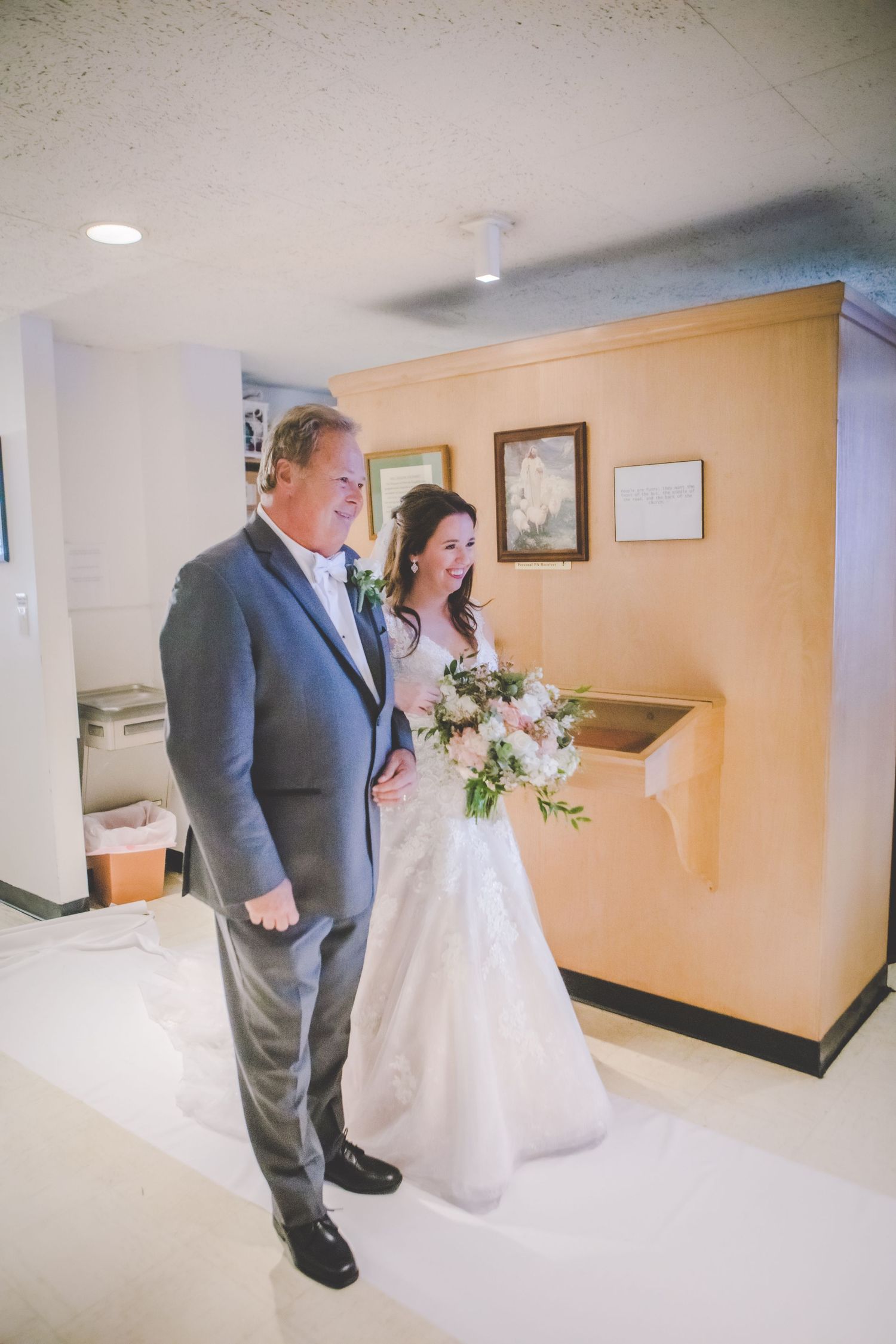 Wedding party members walk through a church corridor with beige walls.