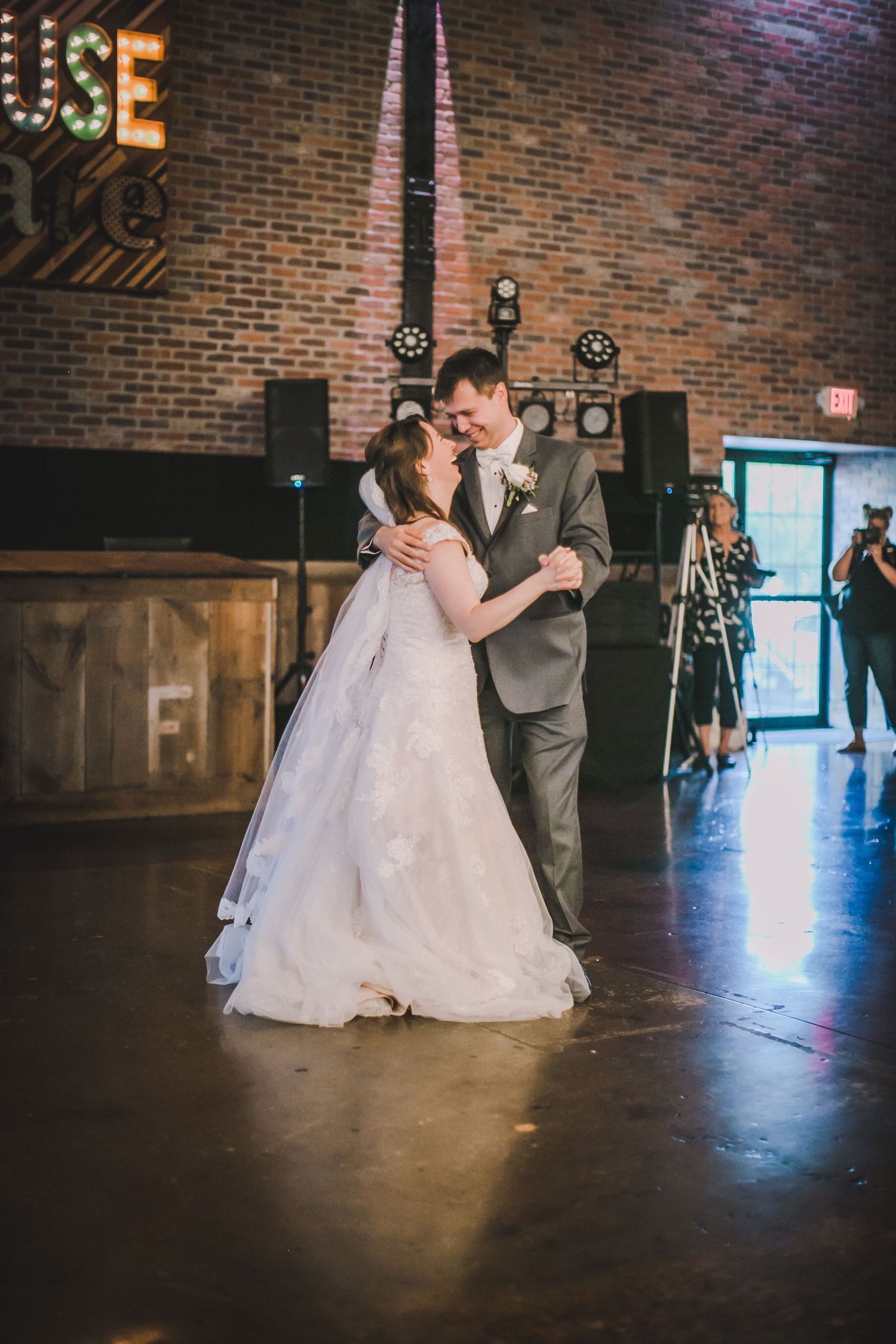 A couple embraces during a dance moment at their wedding reception in a brick-lined venue.