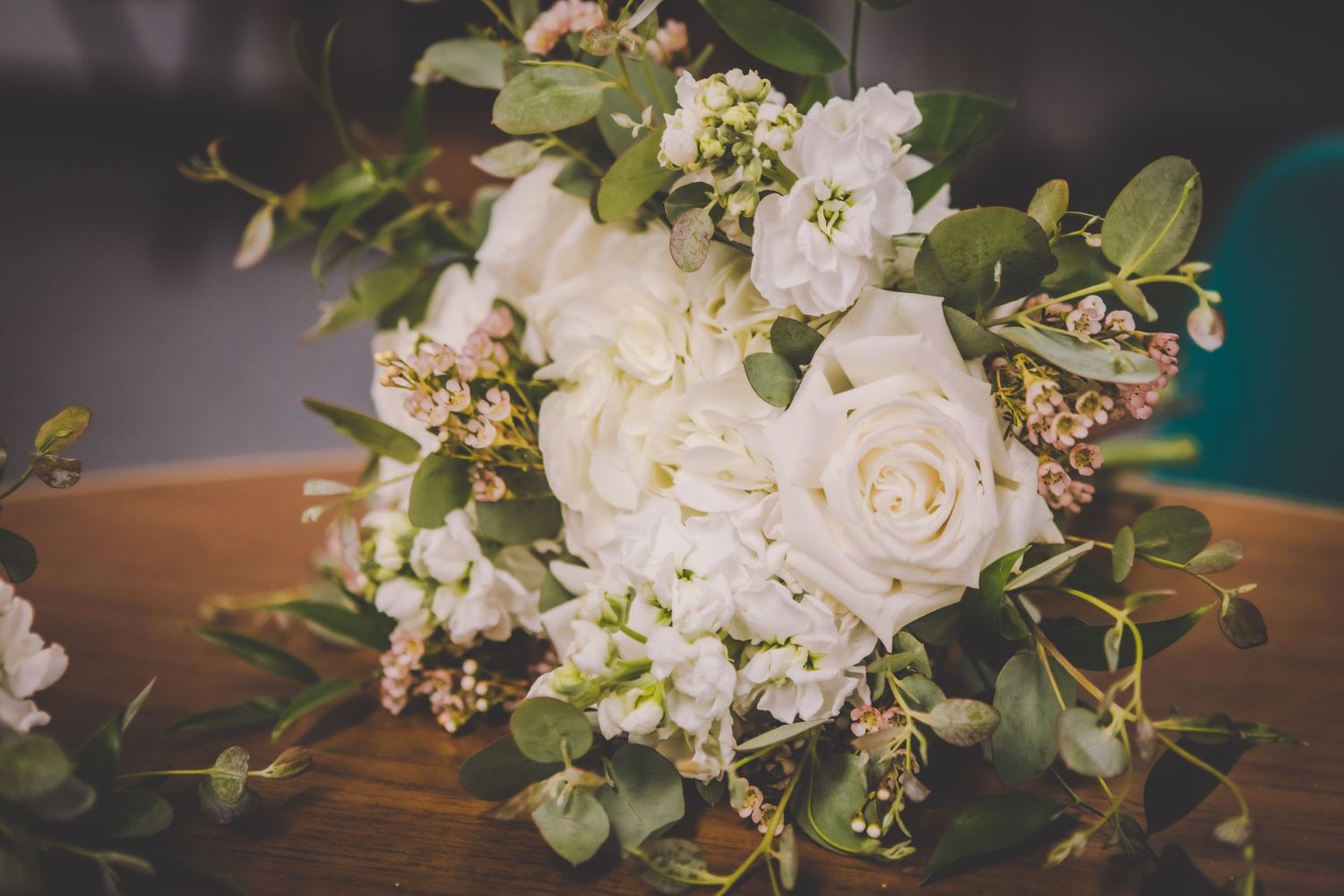 Elegant white rose and eucalyptus wedding bouquet displayed on wooden surface.