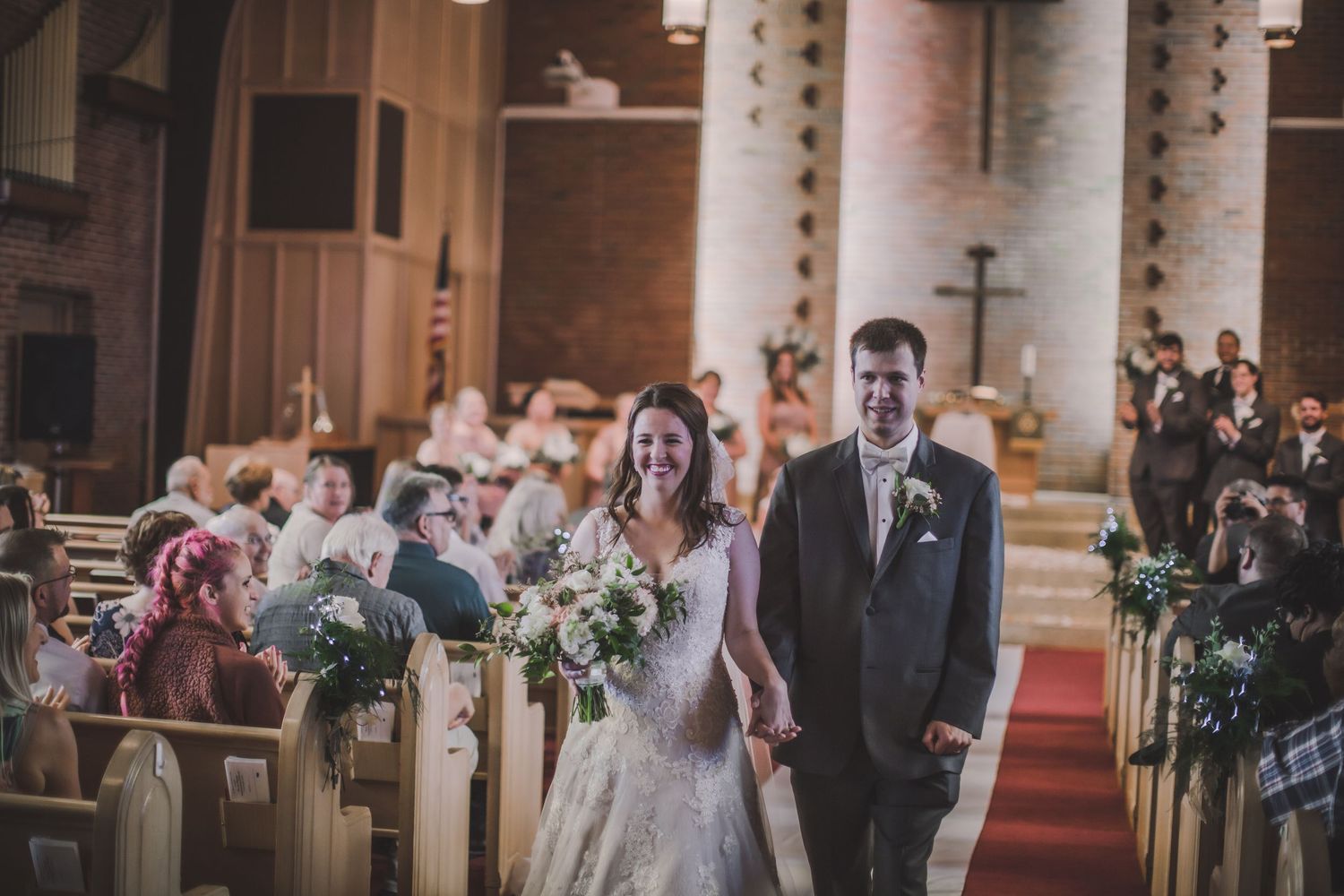 Interior of traditional brick church with white columns and cathedral ceiling during wedding ceremony.