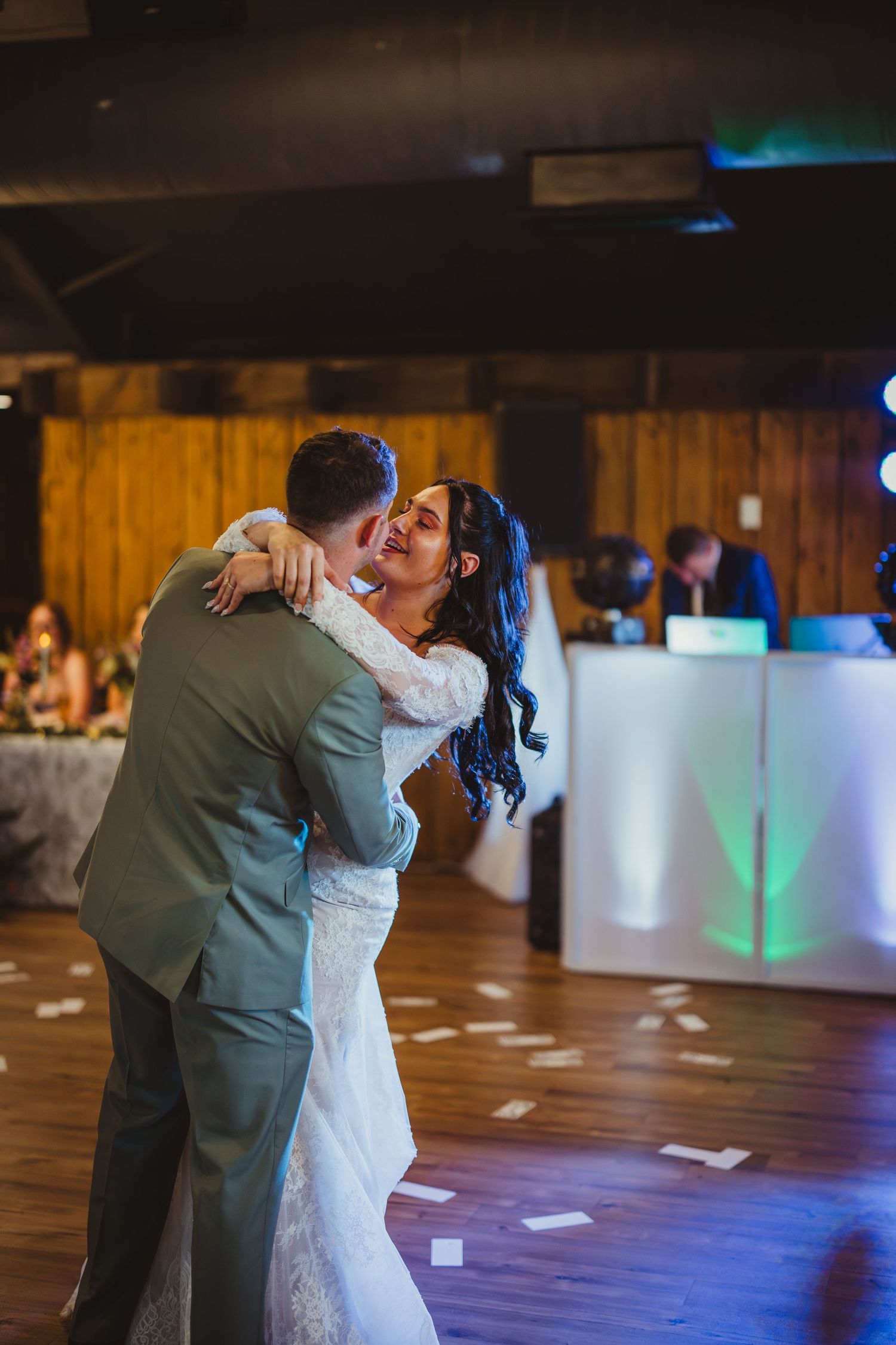 Bride and groom share their first dance, smiling joyfully in a warmly lit wedding reception venue.