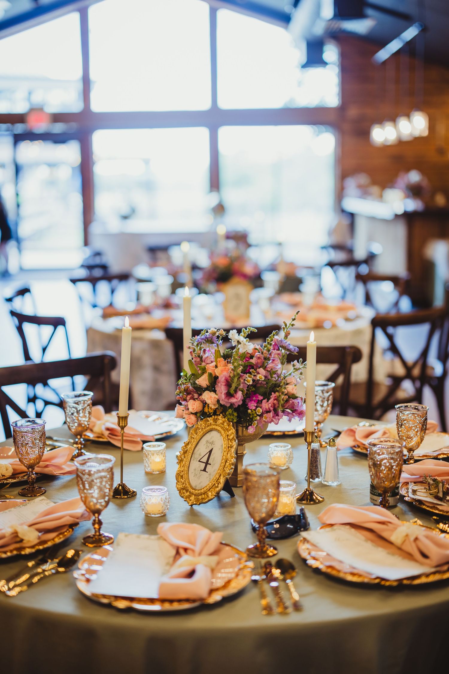 Gold wedding table setting with pink napkins, ornate charger plates, candles, and a floral centerpiece at table four.