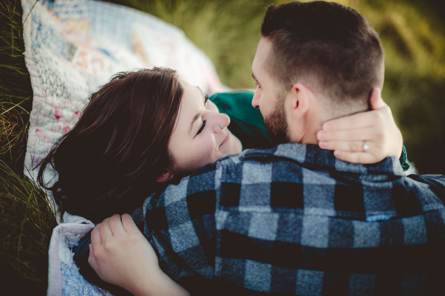 A romantic couple lying on a blanket outdoors sharing an intimate moment in nature.