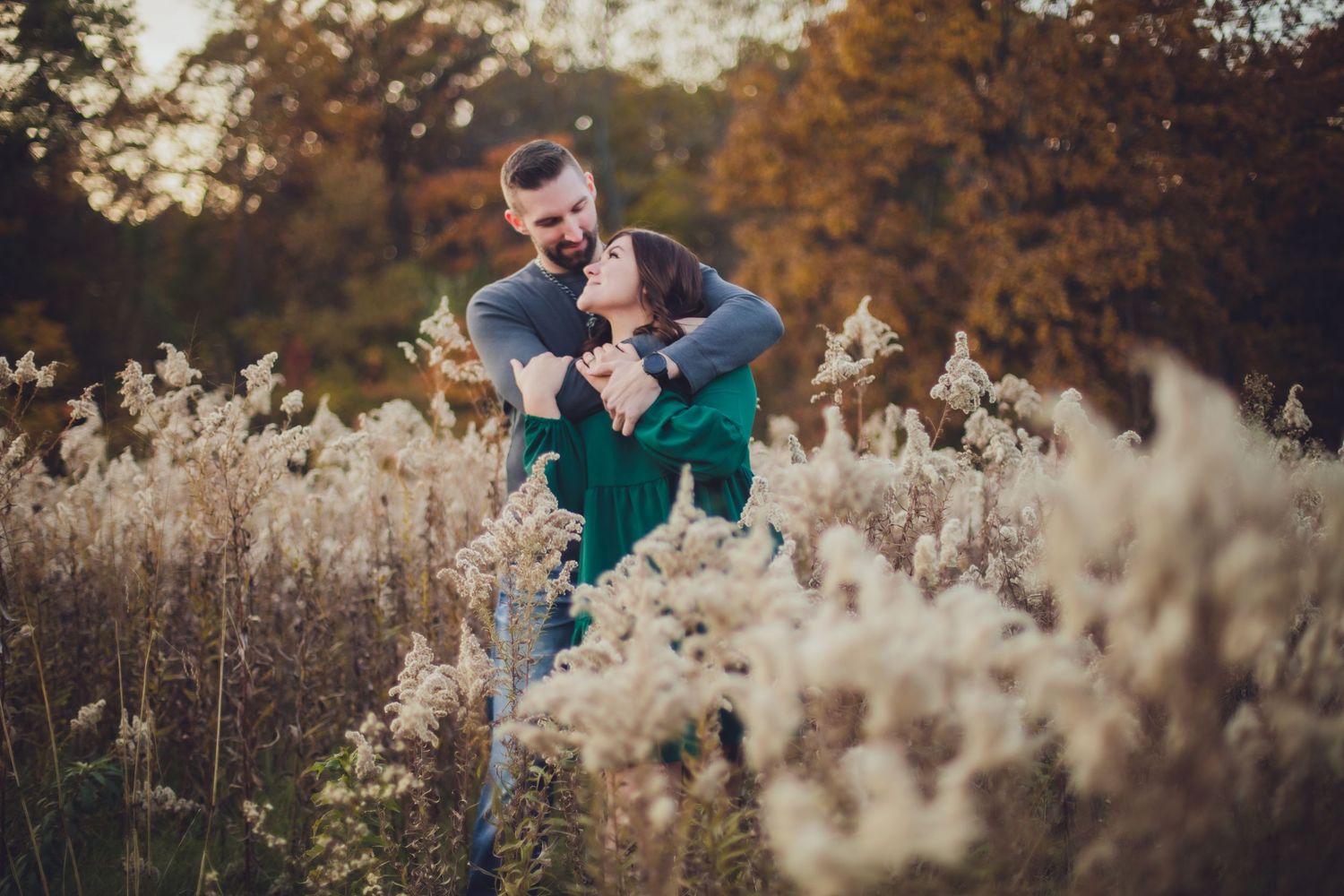 Romantic couple embracing among tall wheat grass during golden hour photoshoot.