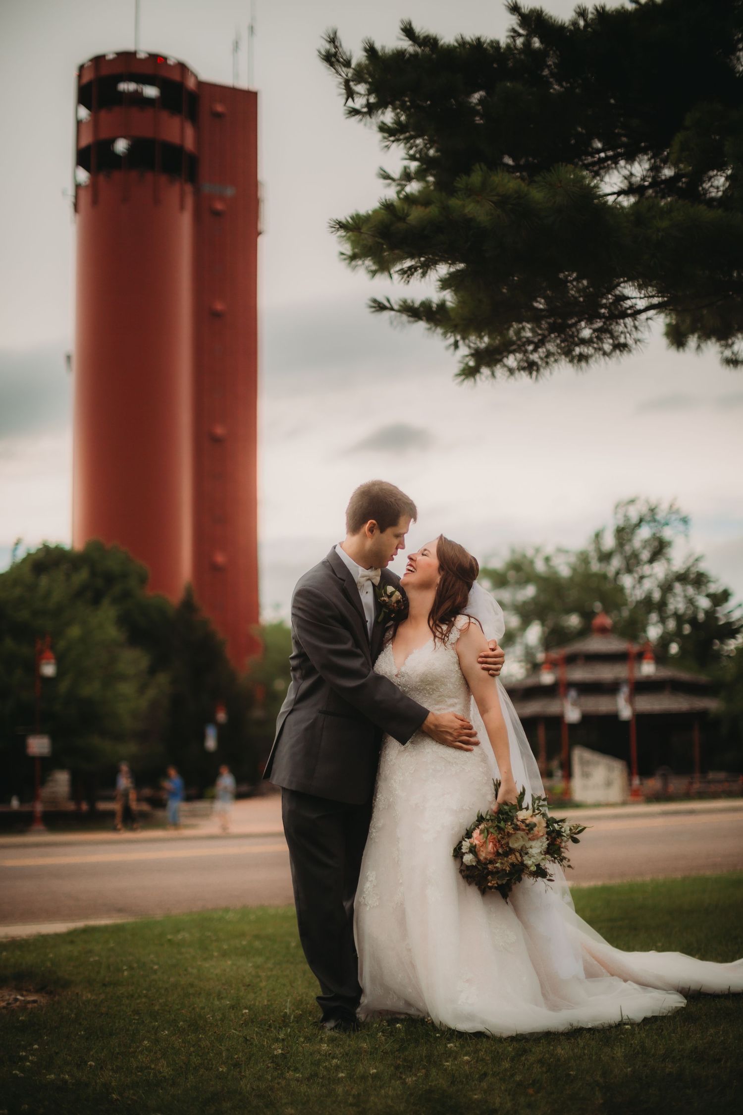 Couple embraces during wedding photoshoot with dramatic red tower in background.