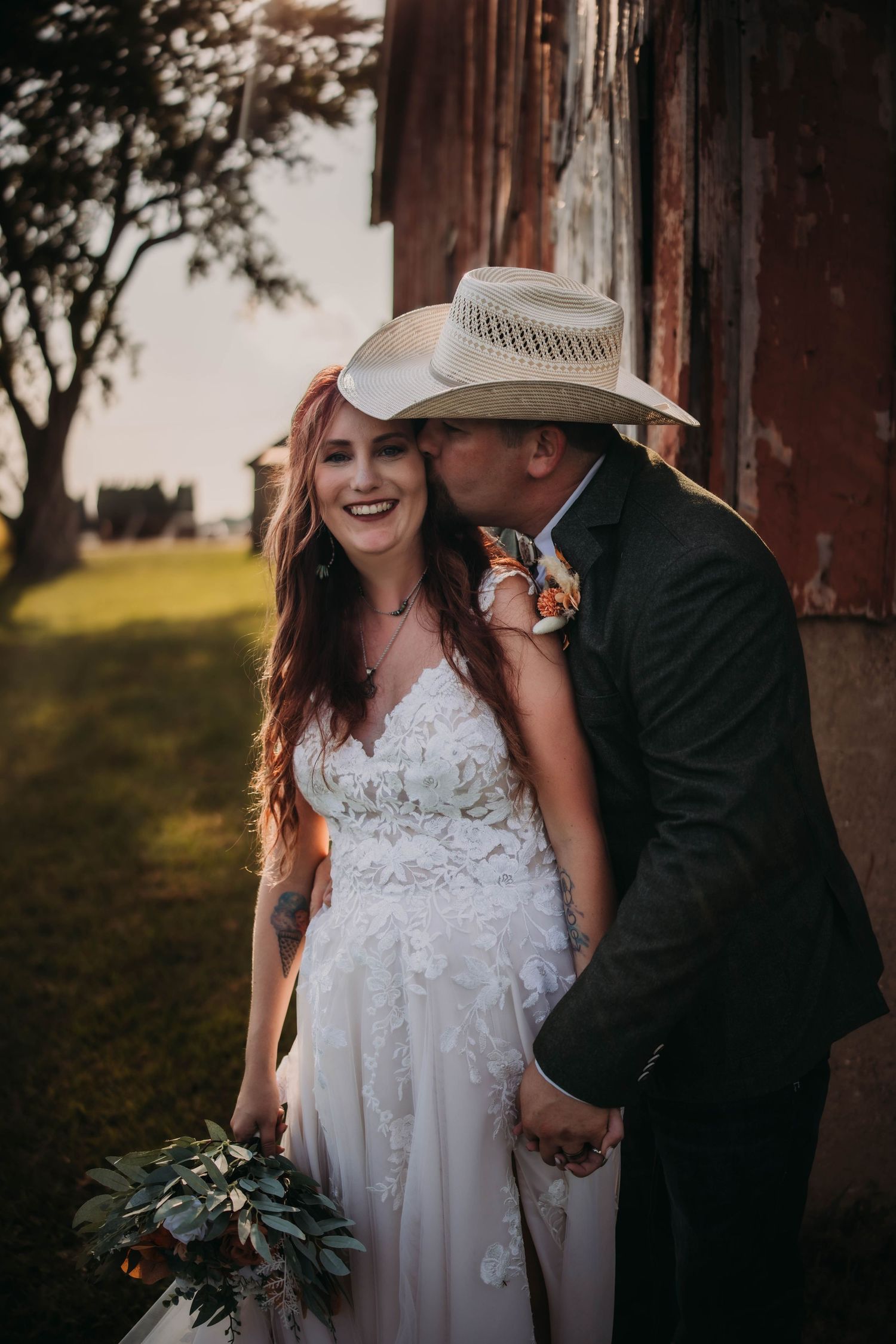 Joyful newlyweds share an intimate moment outside a rustic barn on their wedding day.