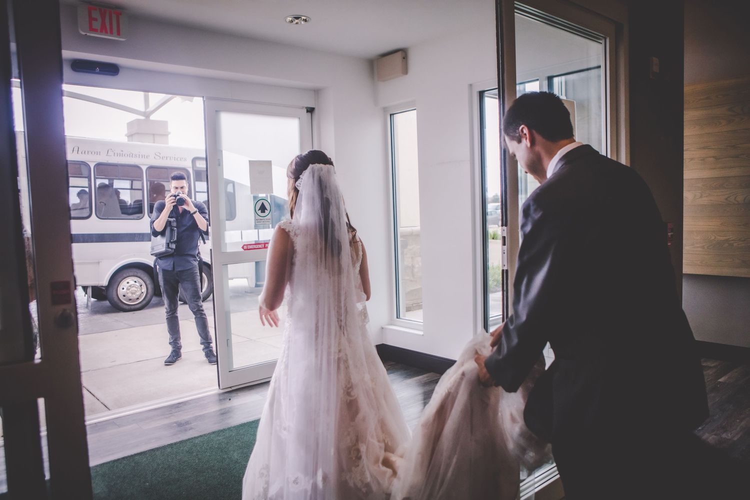 Wedding party entering through glass doors of a building lobby.
