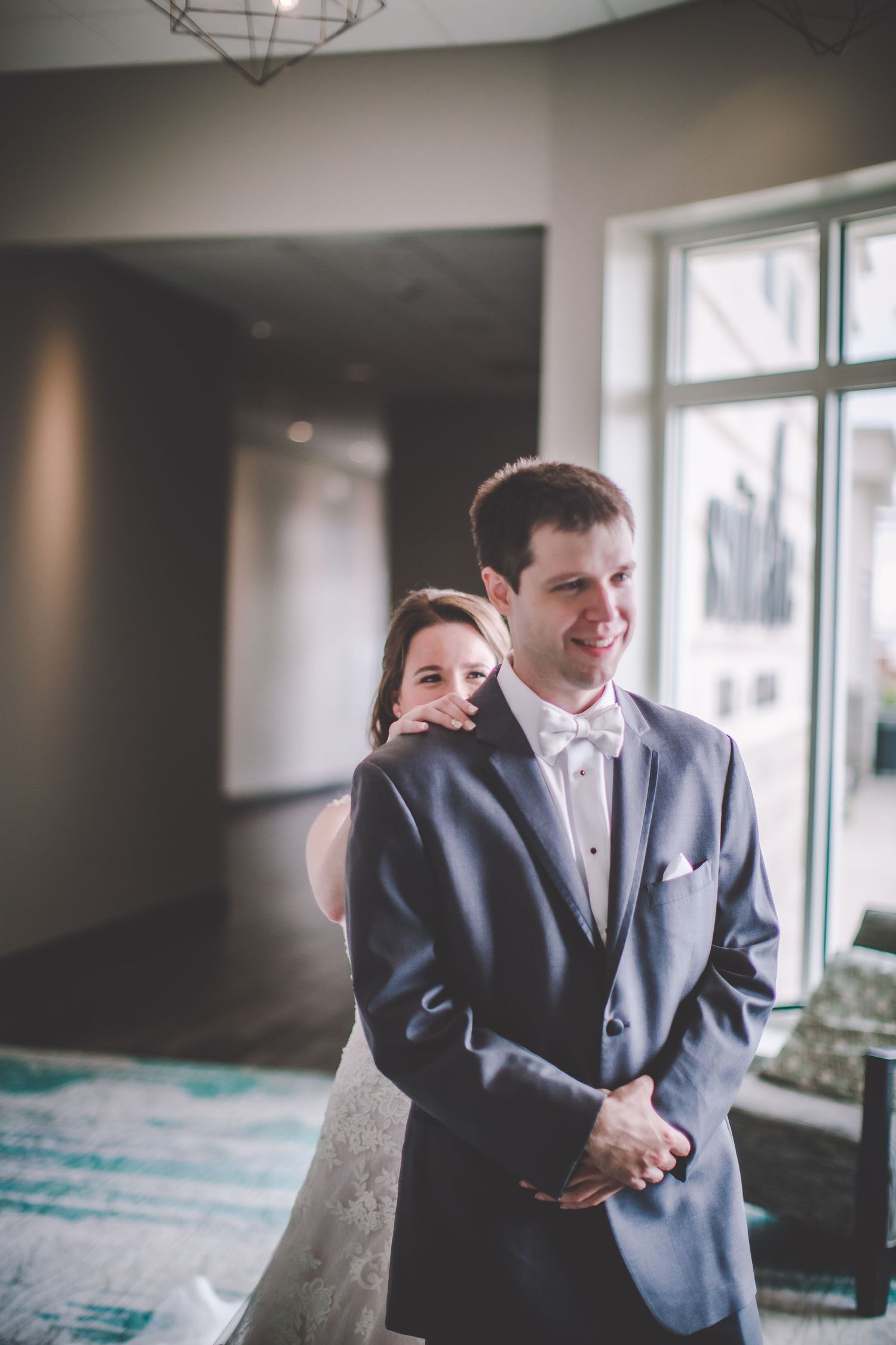 Intimate indoor moment between newlyweds showcasing grey suit and white wedding dress.