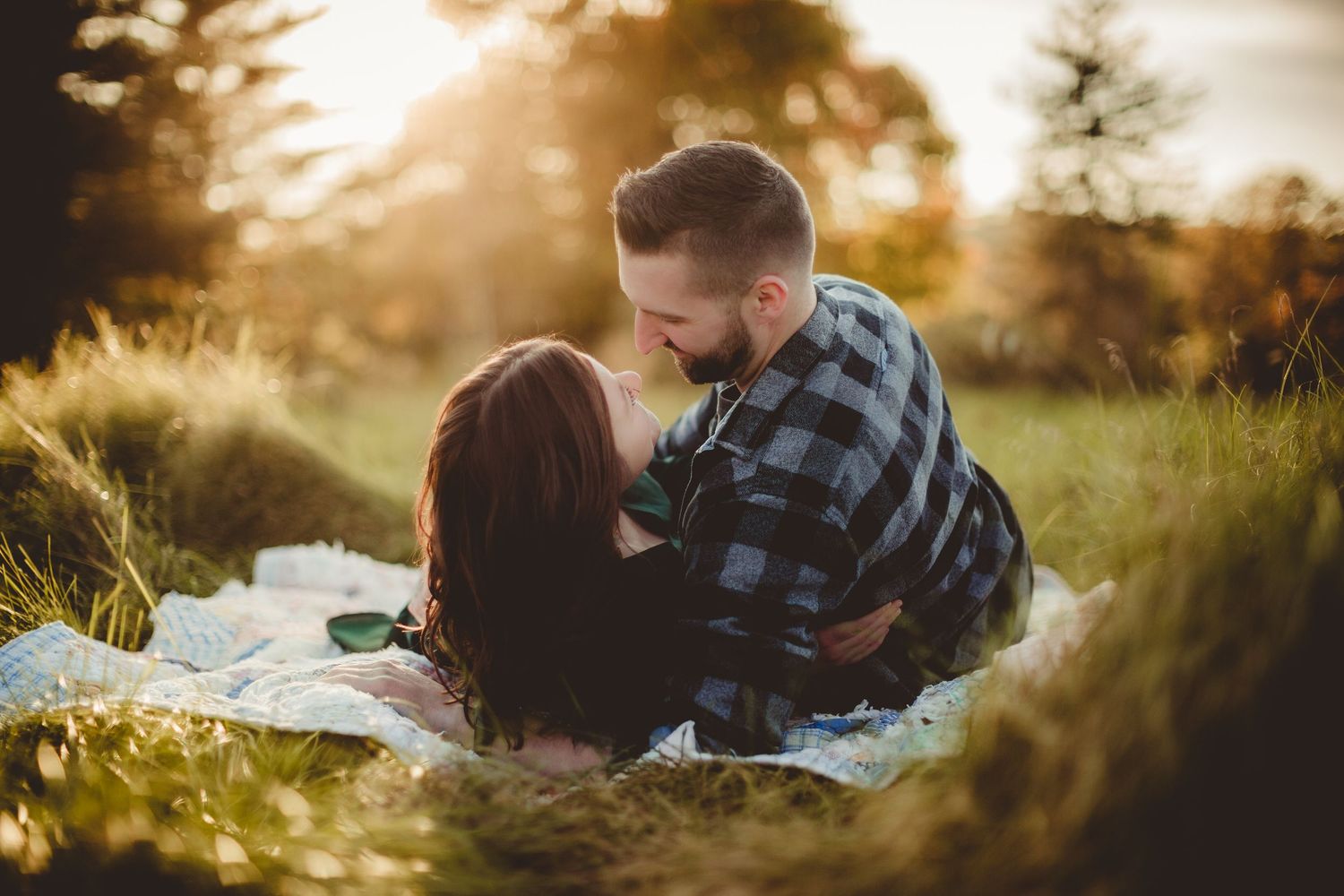 A couple shares tender moments on a blanket during sunset in a natural setting.