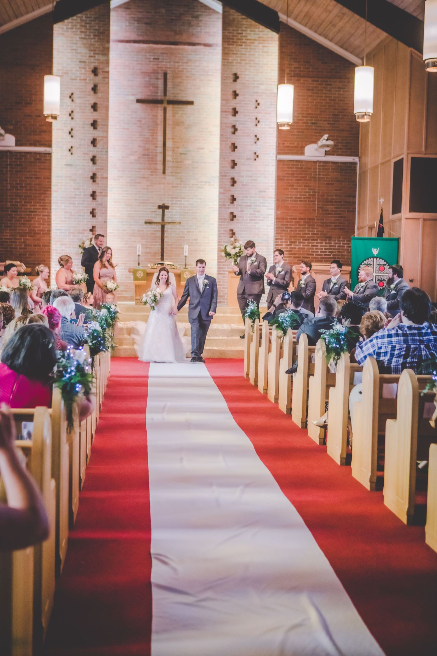 Wide angle view of wedding guests seated in wooden church pews during ceremony.