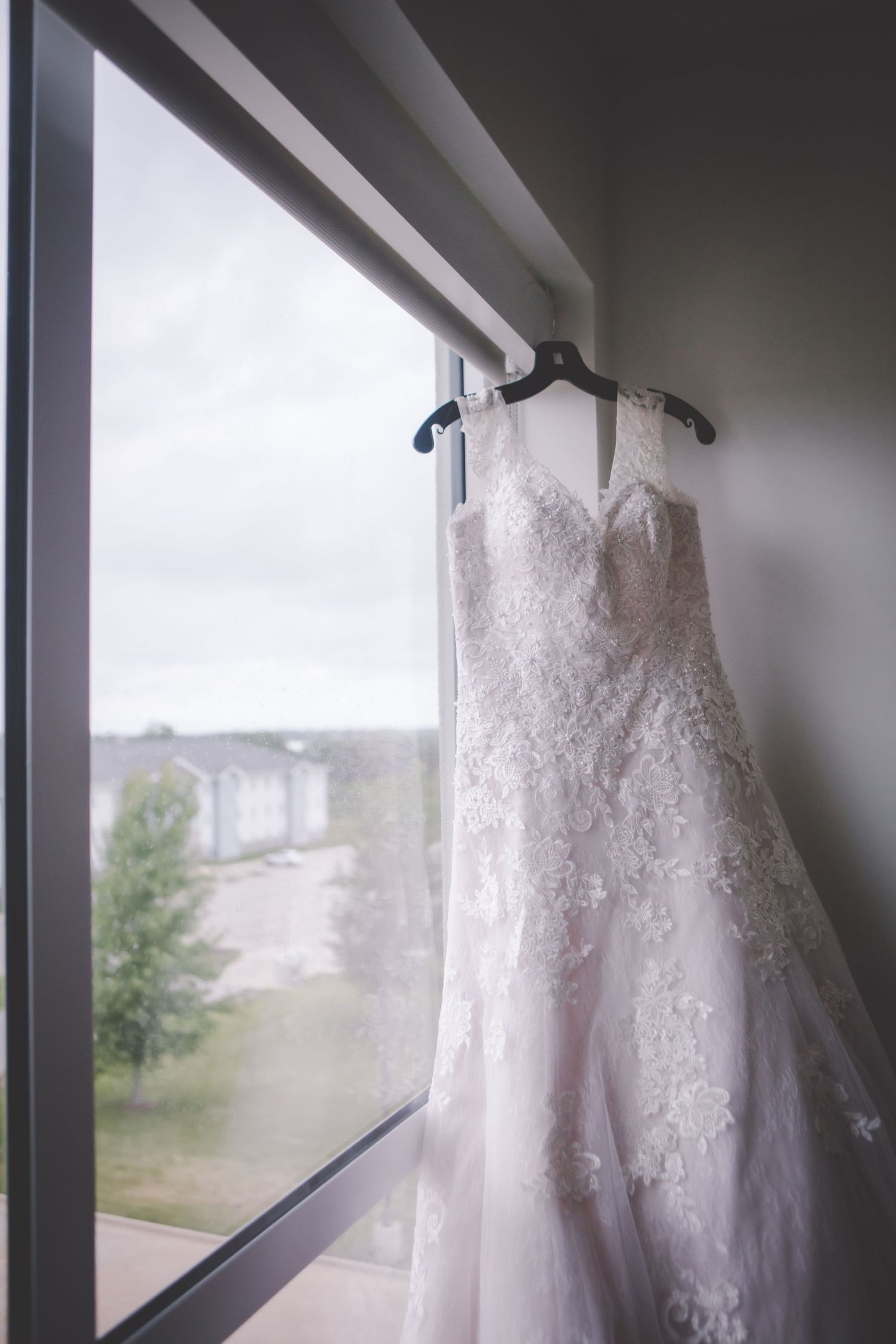 Elegant white lace wedding dress hanging in front of a window with natural light streaming in.