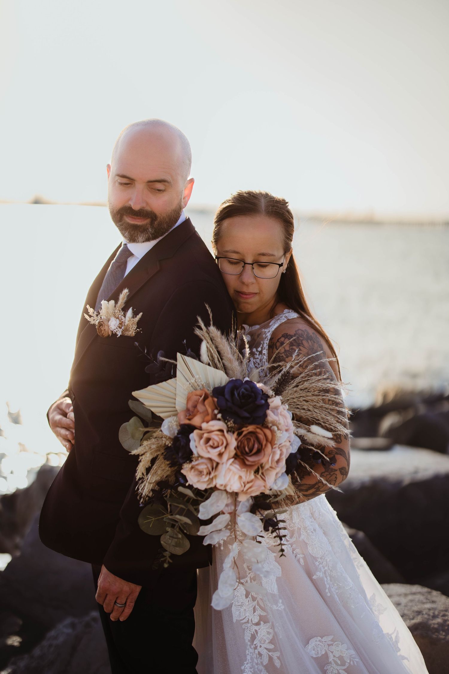 Romantic beach wedding scene with couple holding beautiful pink and purple floral bouquet at sunset.