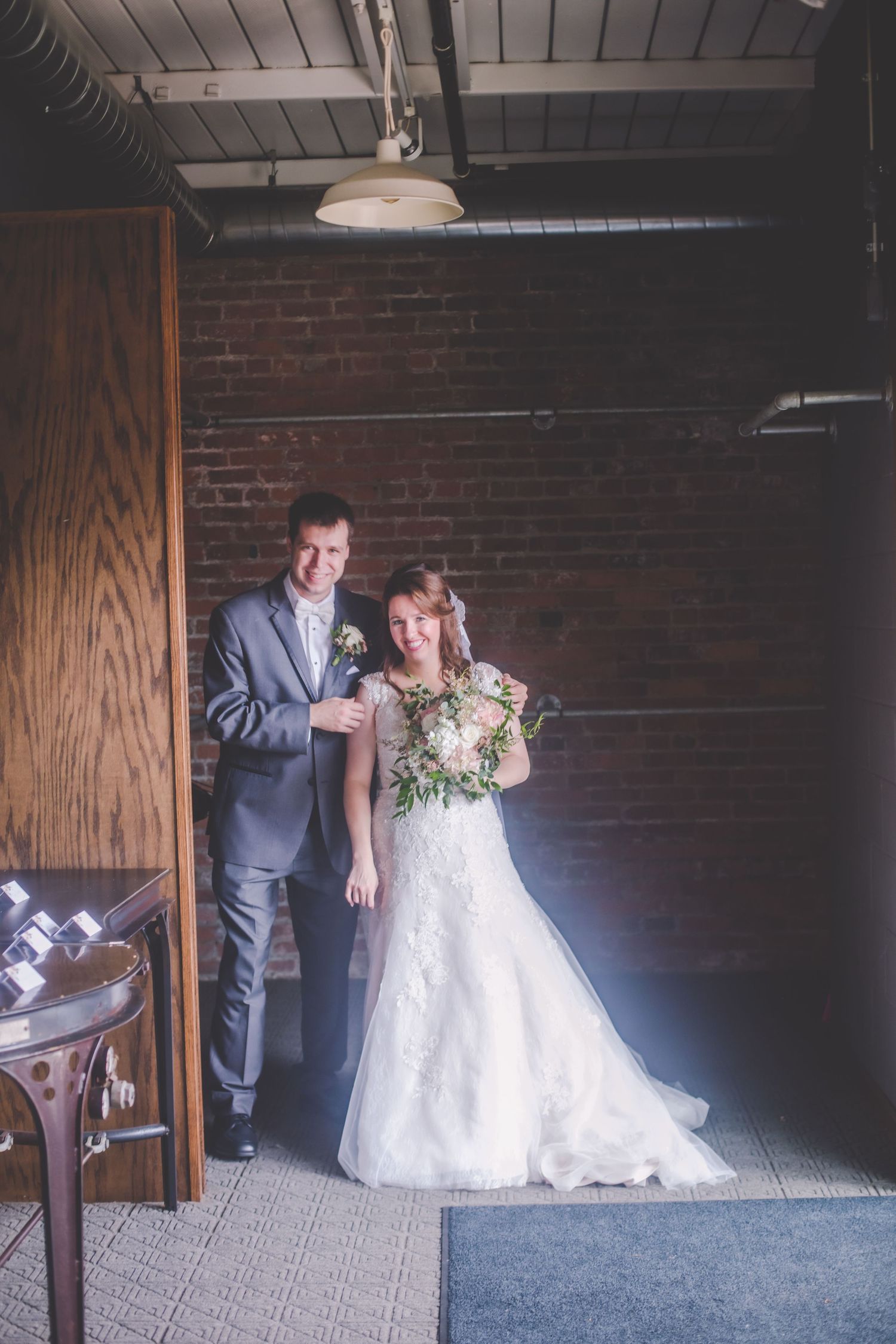 Couple poses for portrait against rustic brick wall in wedding attire.