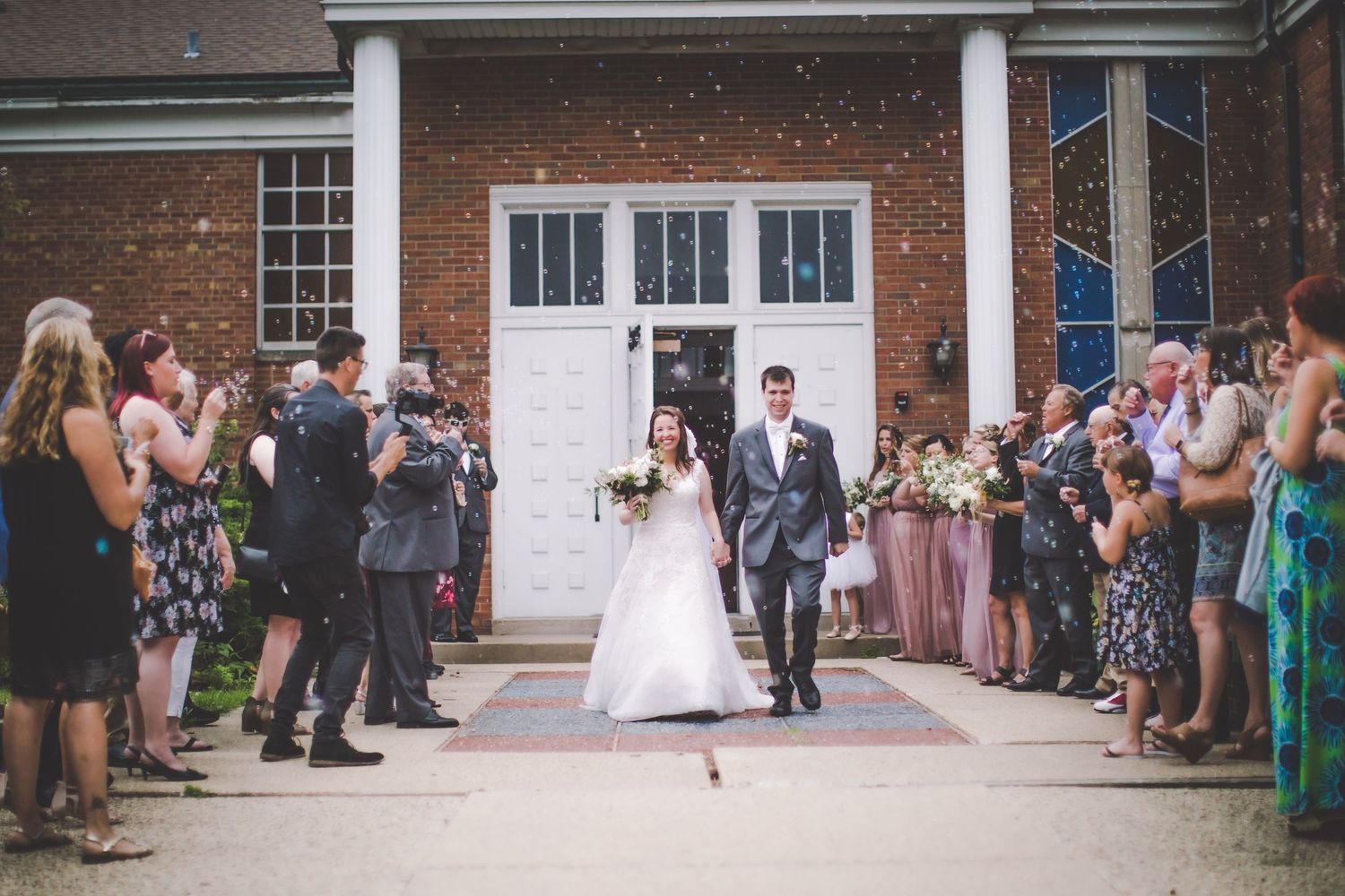 Wedding celebration scene with guests lining pathway at brick venue entrance.