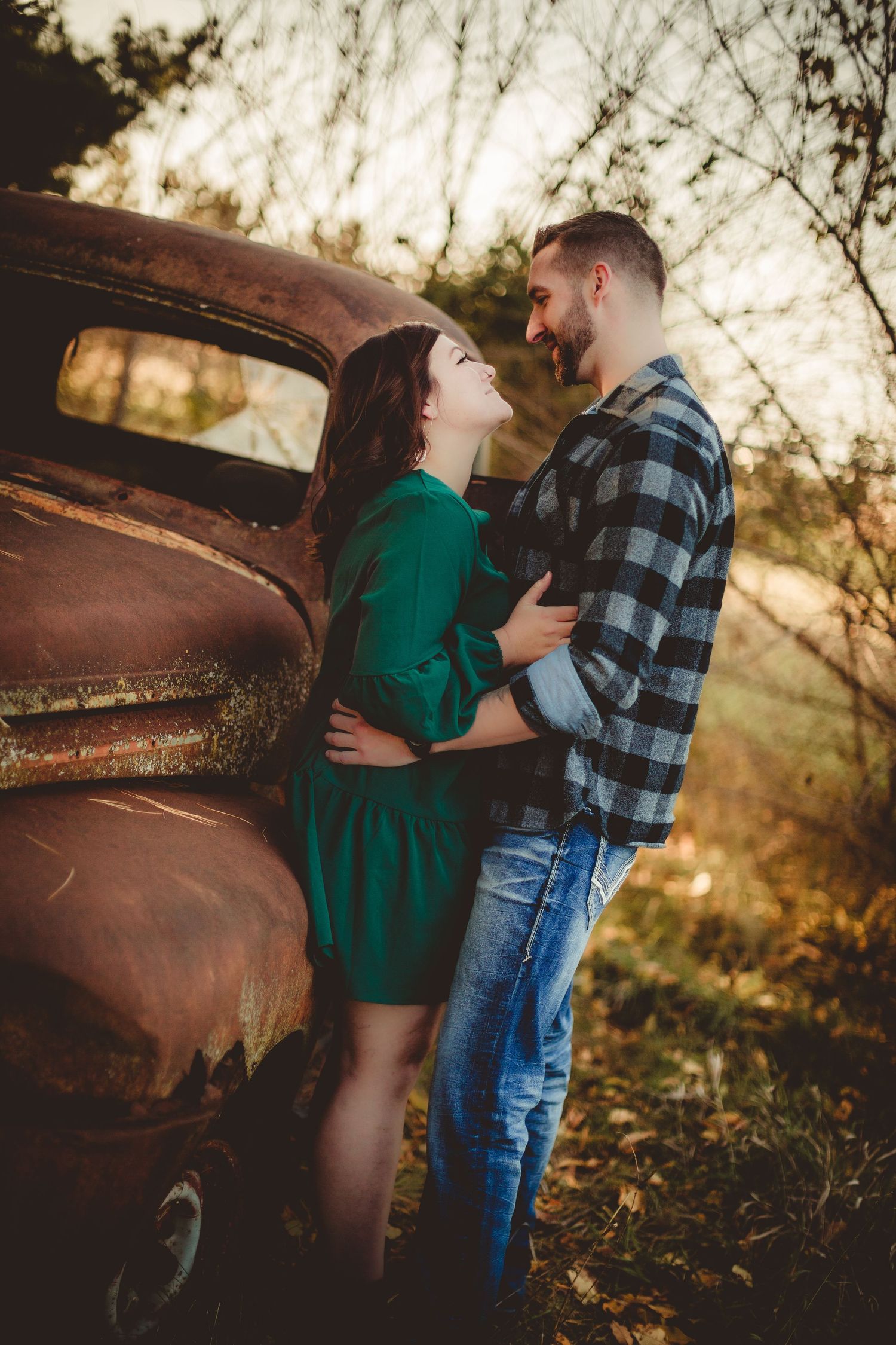 Couple poses by vintage rusty truck wearing plaid shirt and green dress.