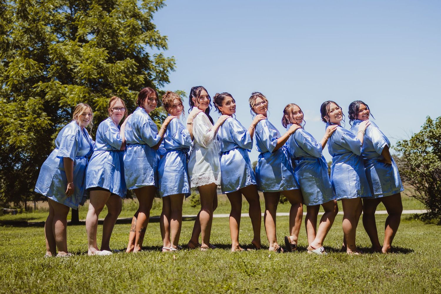 Bridesmaids and bride posing outdoors in matching blue robes and white bridal robe on a sunny day.