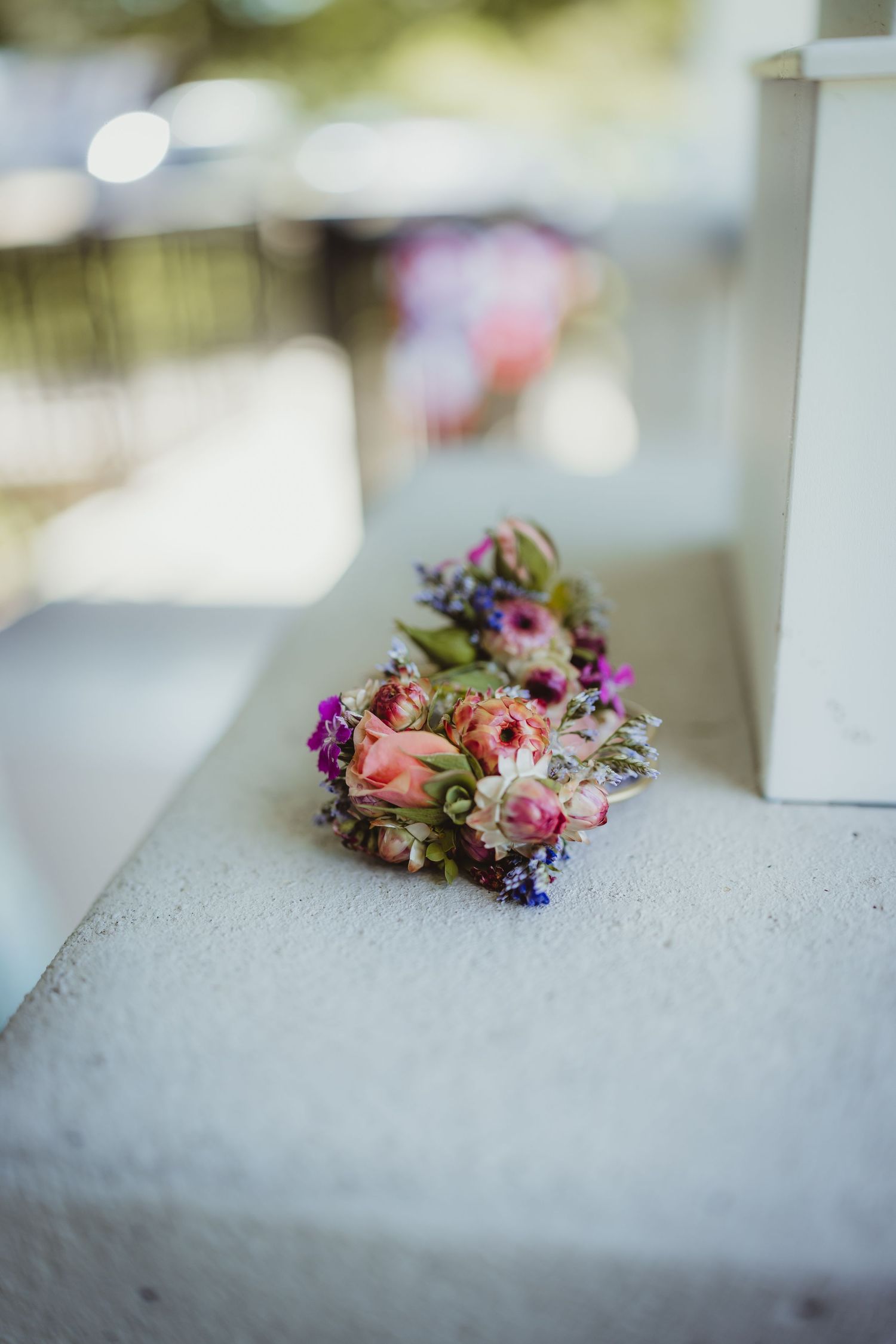 Small floral boutonniere with pink roses and purple wildflowers resting on a white concrete ledge.