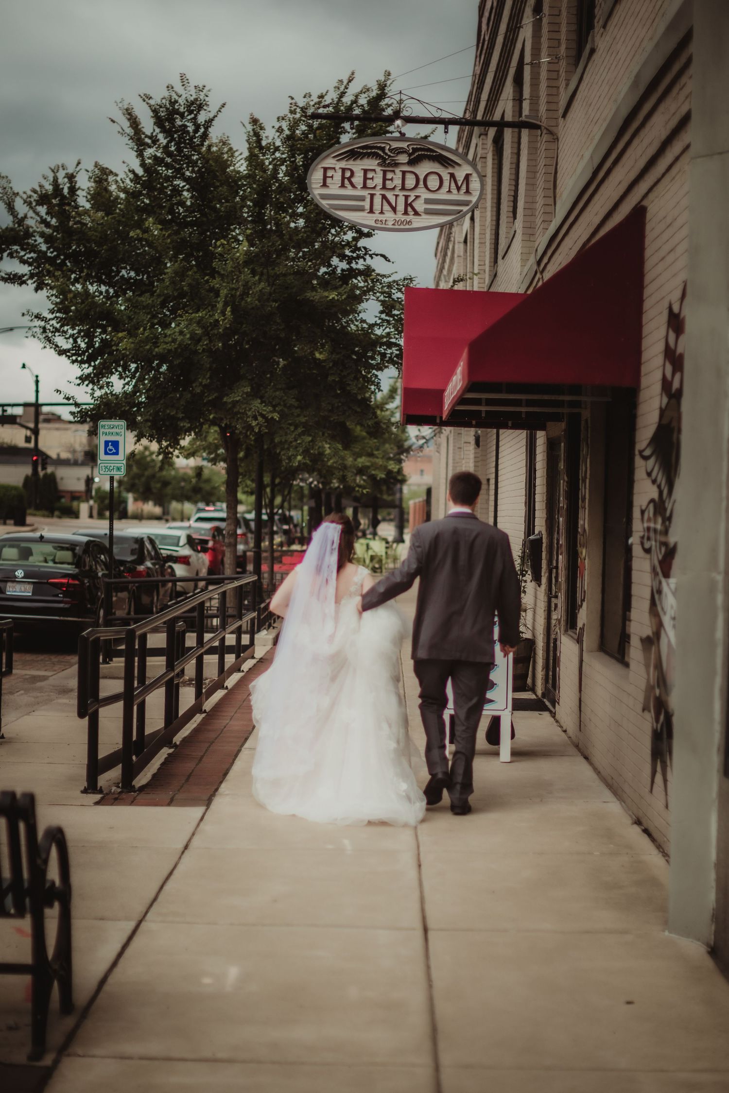 Wedding couple strolls past Freedom Ink sign on city street with red awning.