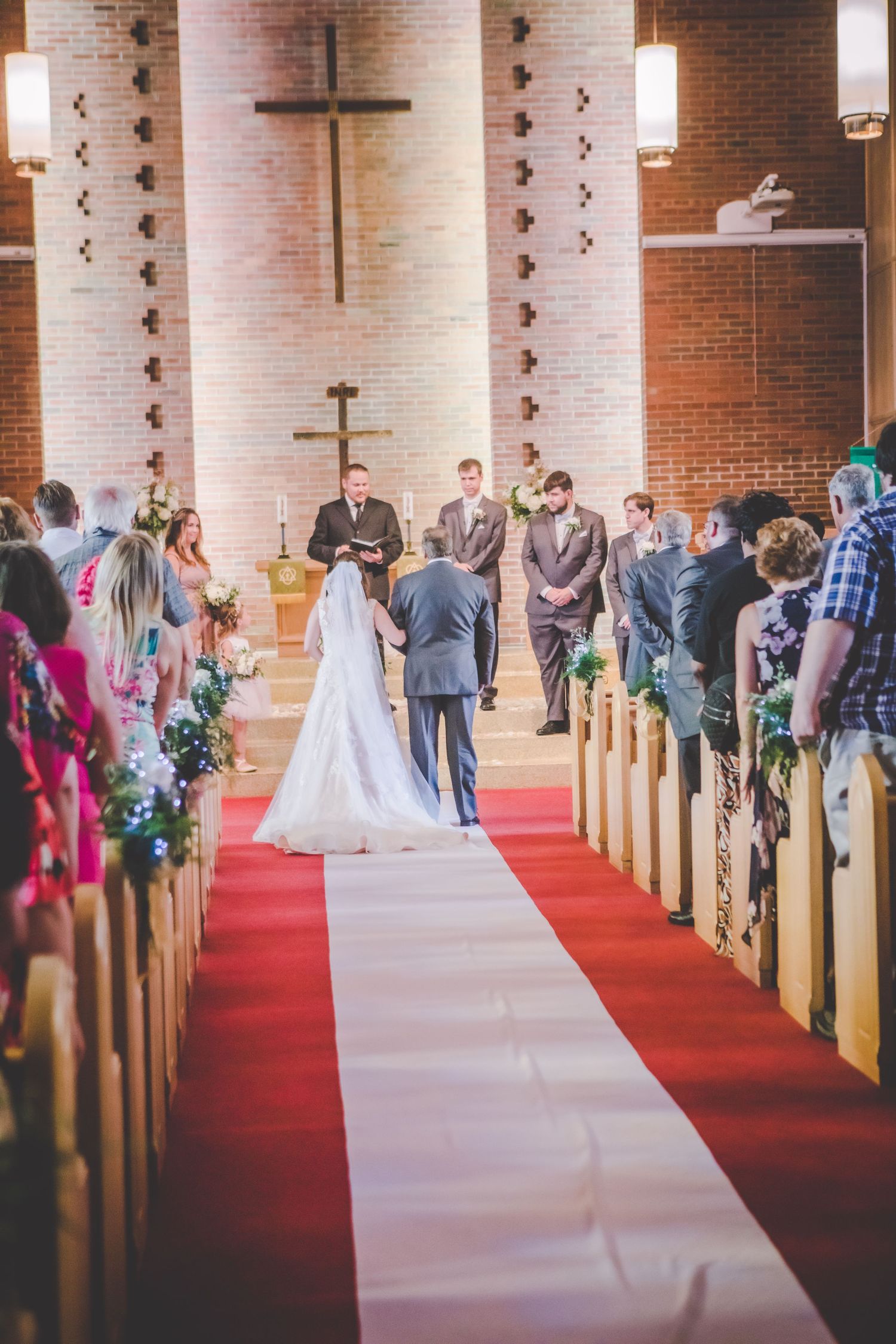 A wedding ceremony takes place in a church with exposed brick walls and decorative cross centerpiece.