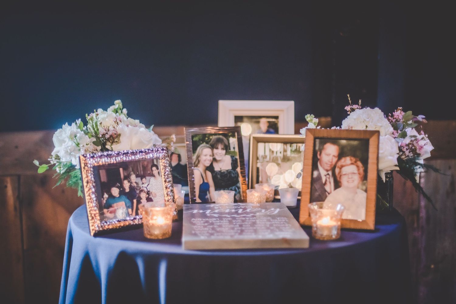 Wedding memory table with framed photographs and floral decorations illuminated by candlelight.