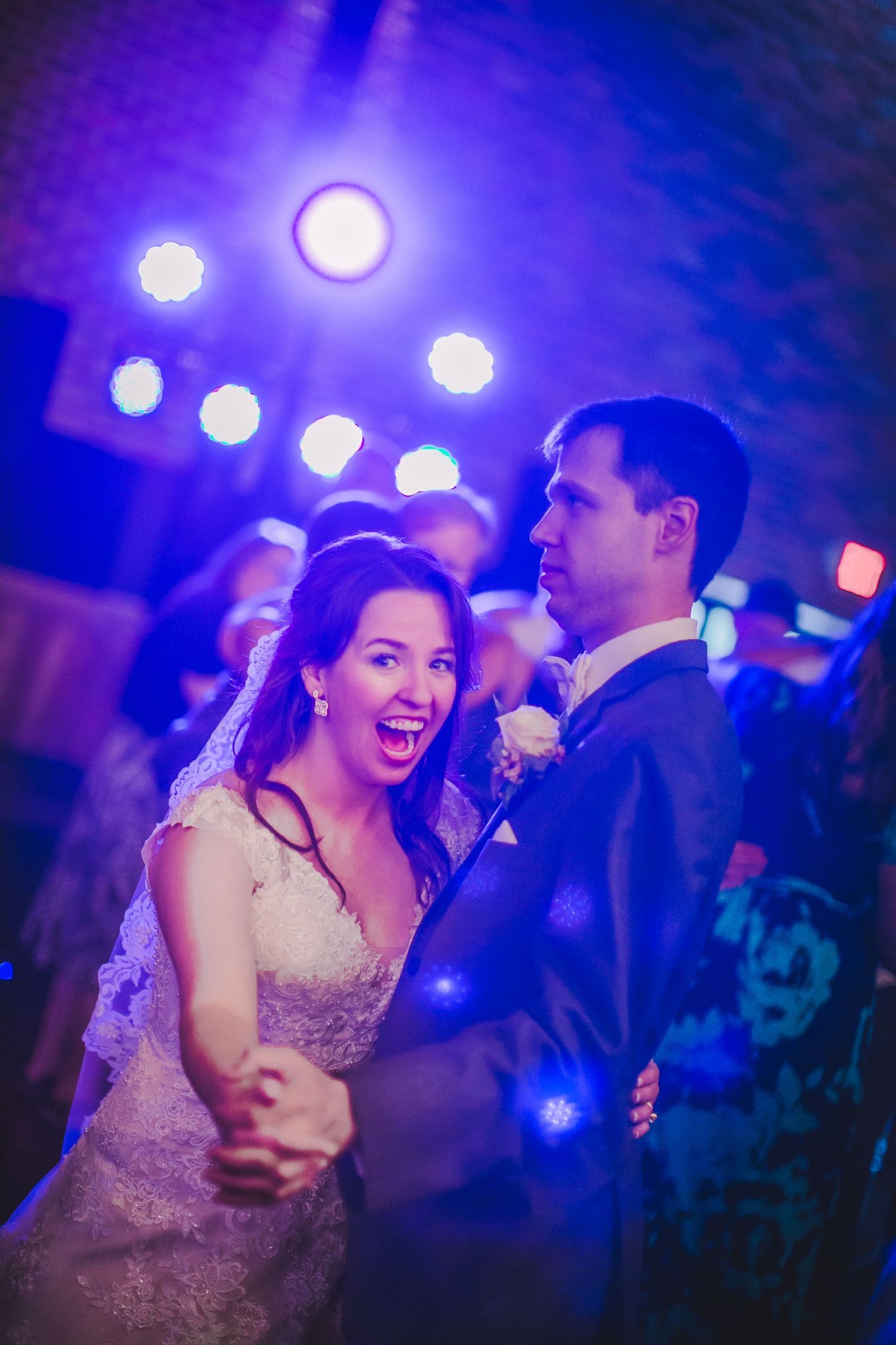 A couple shares a lively dance moment under vibrant purple lighting at their reception.