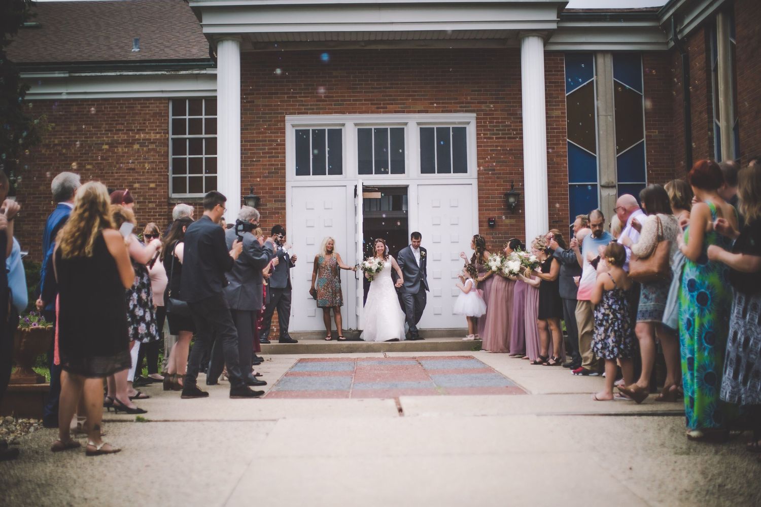 Wedding attendees lined up along brick church exterior waiting for newlyweds.
