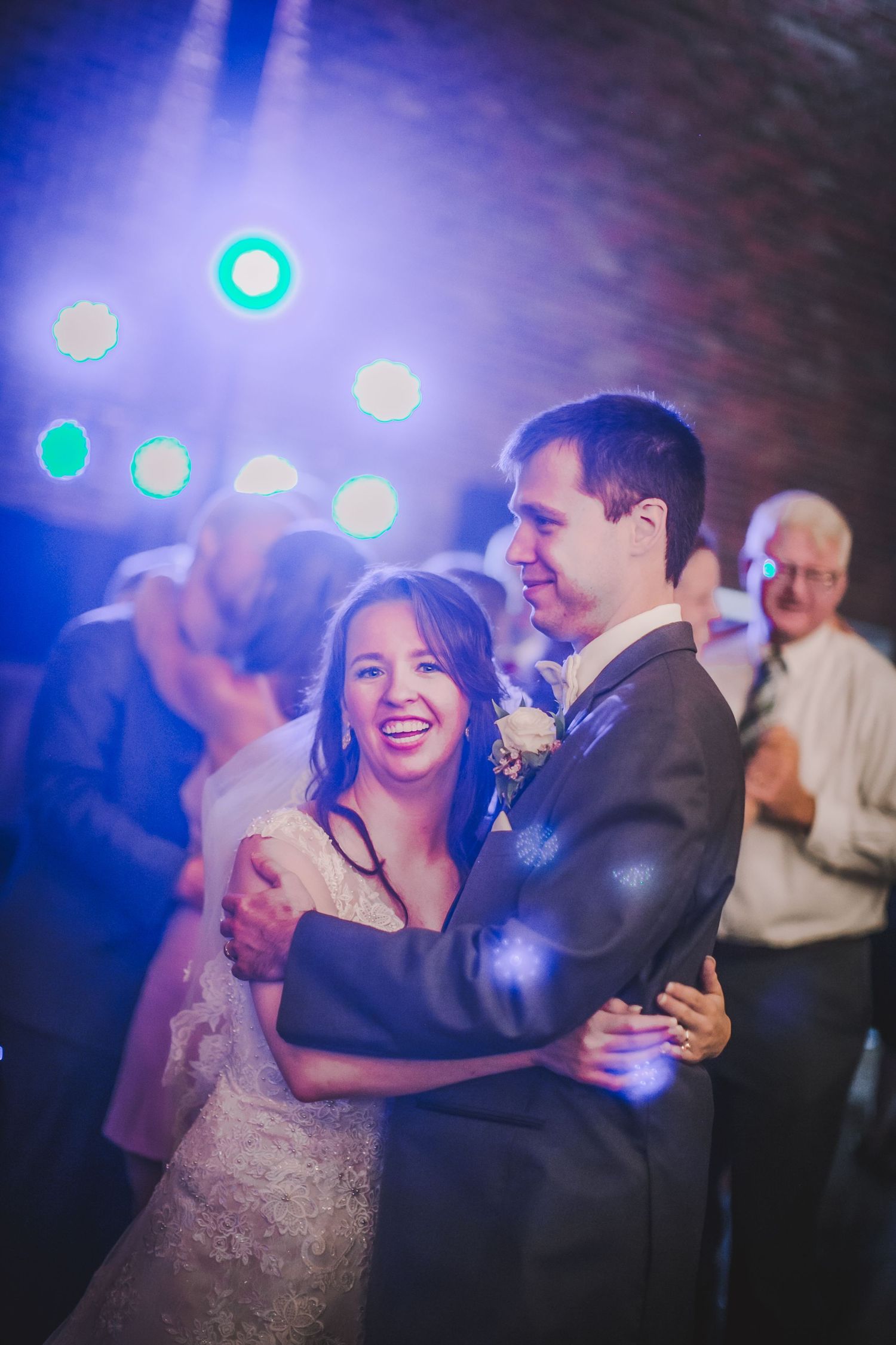 A joyful dance moment captured under blue reception lighting at a wedding celebration.