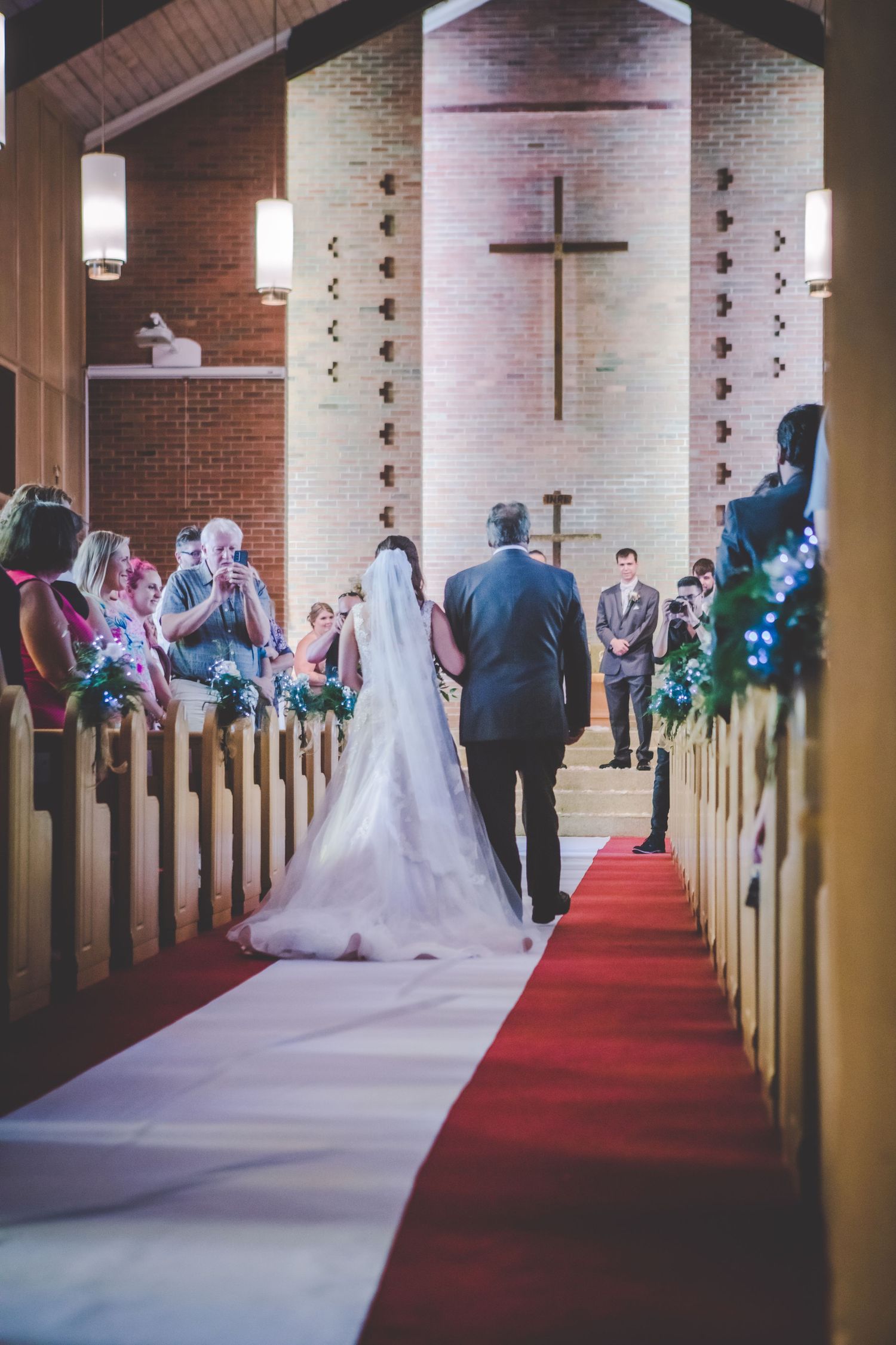 A wedding ceremony in progress inside a brick church with wooden pews and red carpet aisle.
