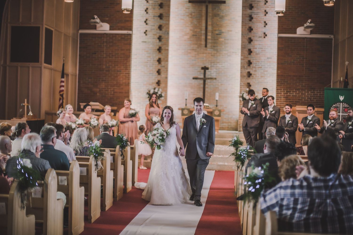 Elegant church wedding ceremony showing guests seated in wooden pews with red carpet aisle and floral arrangements.